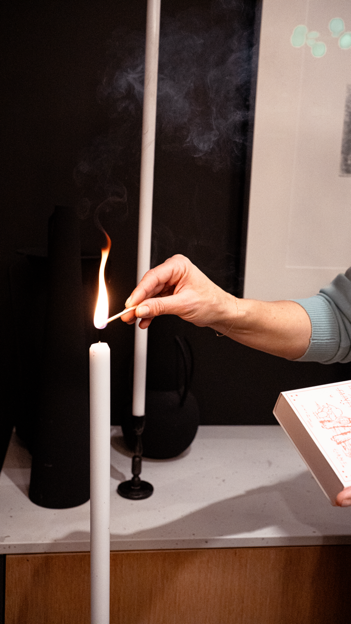 A person is lighting a white candle with a match in a dimly lit room.