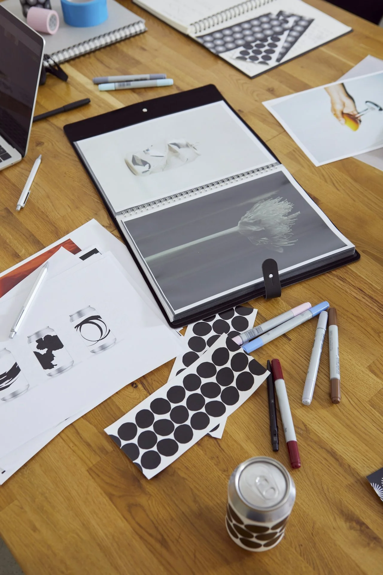 Table with various design and art books, sketches, pattern papers, pens, and a can with a black and white circular pattern.