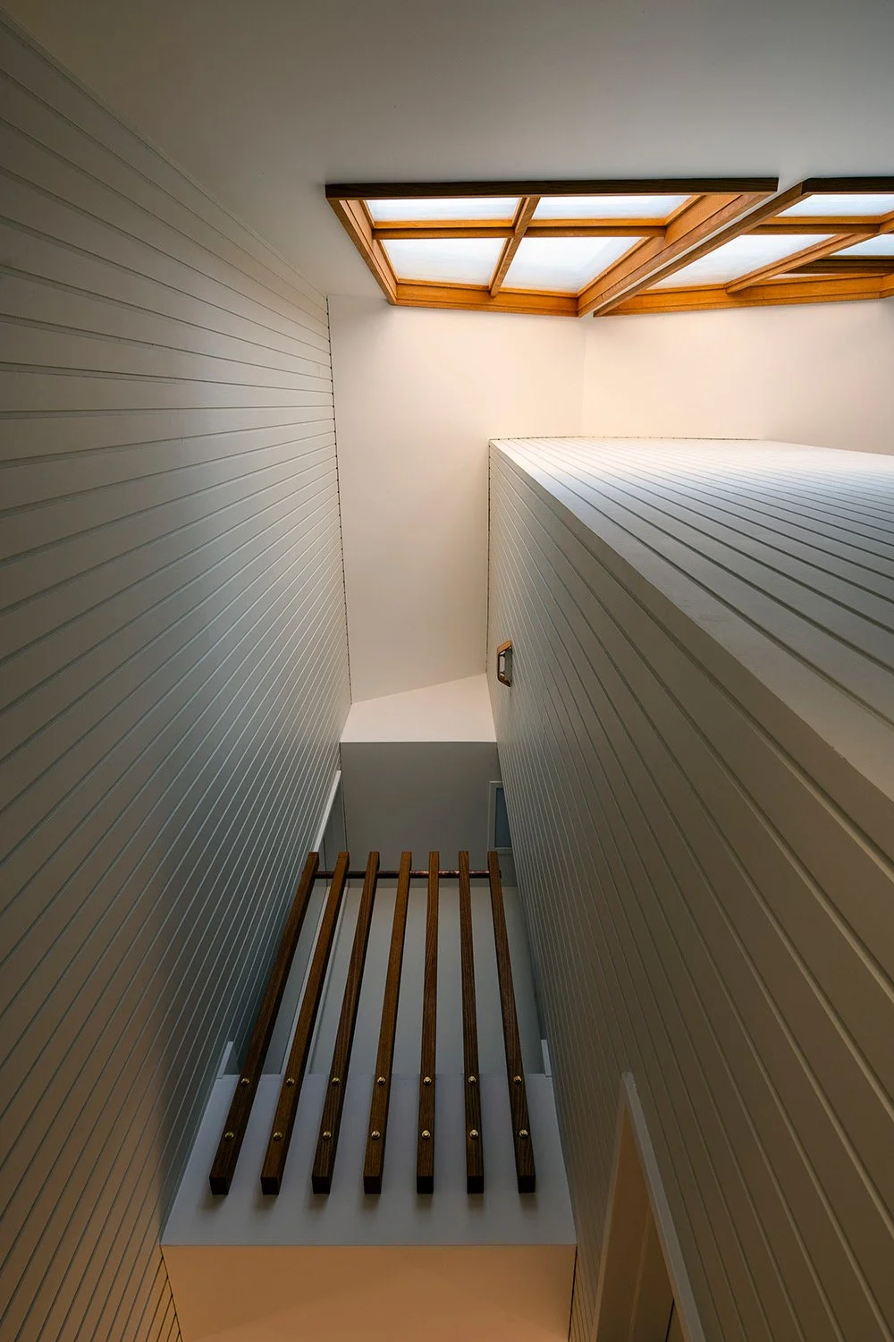 Interior view of a narrow staircase with white paneling walls leading to a skylight.
