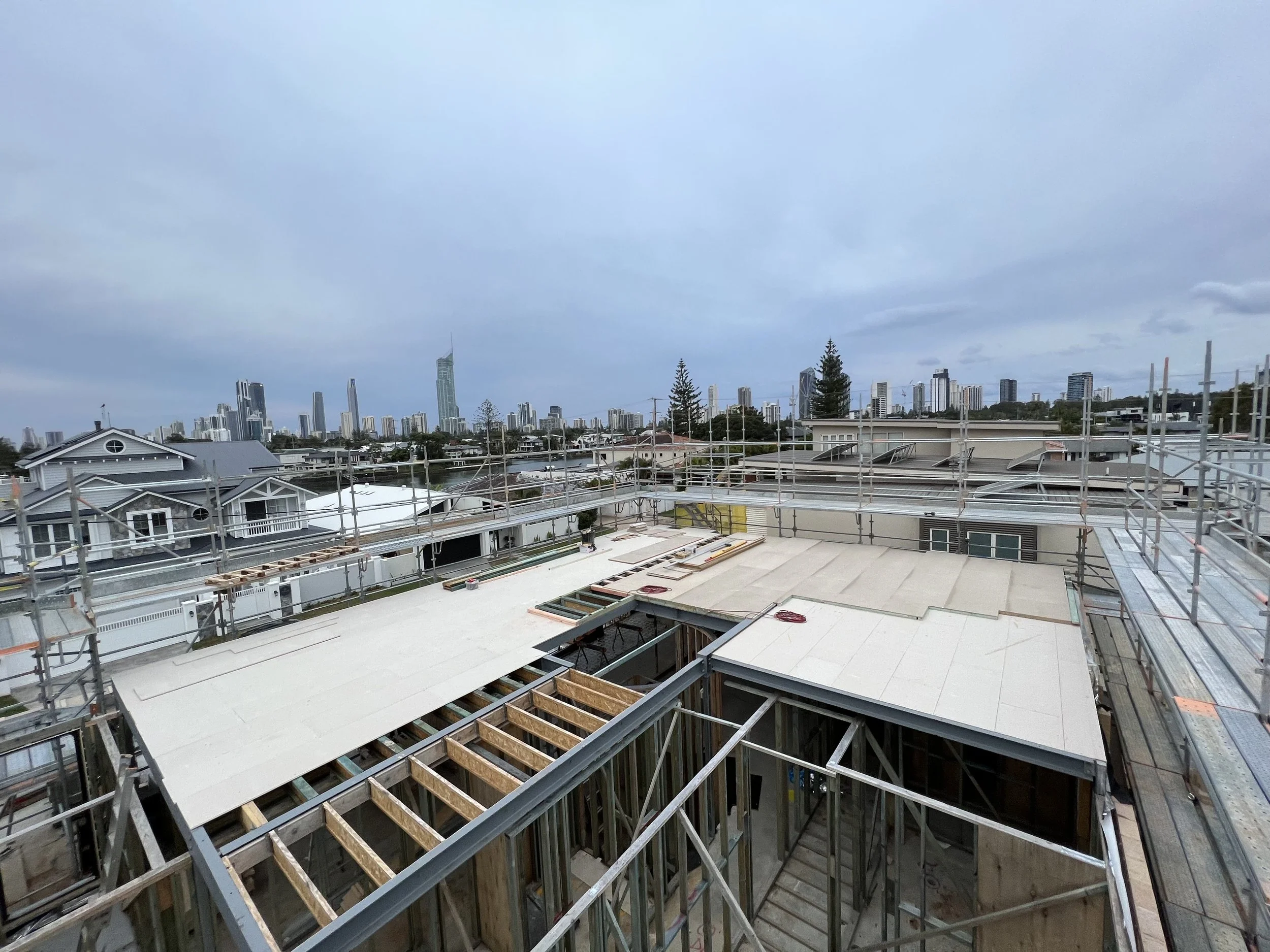 Gold coast Construction site on a building roof with scaffolding, wooden beams, and construction materials, overlooking a city skyline with tall skyscrapers under a cloudy sky.