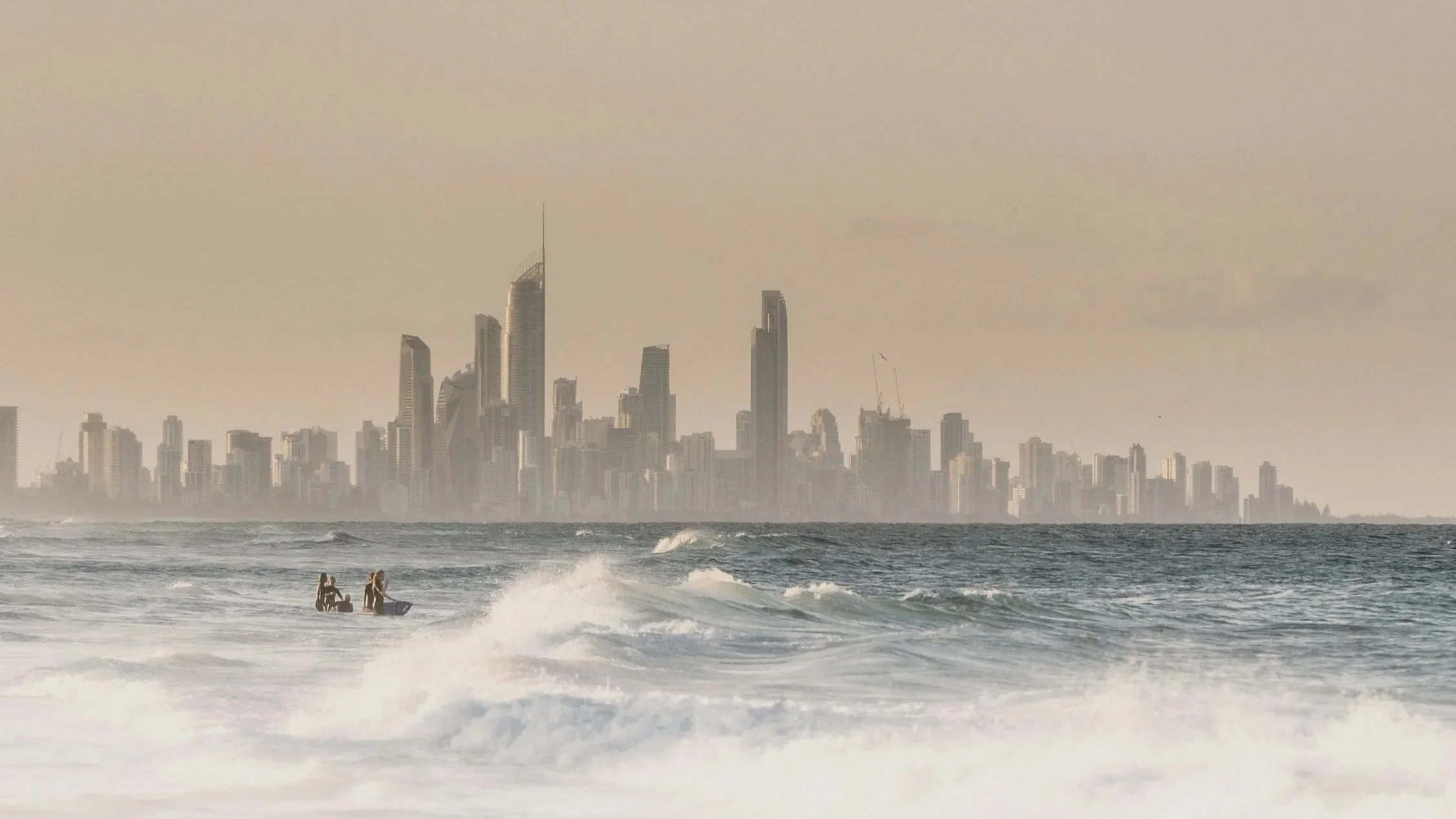 People surfing in the ocean with a city skyline in the background during the day.