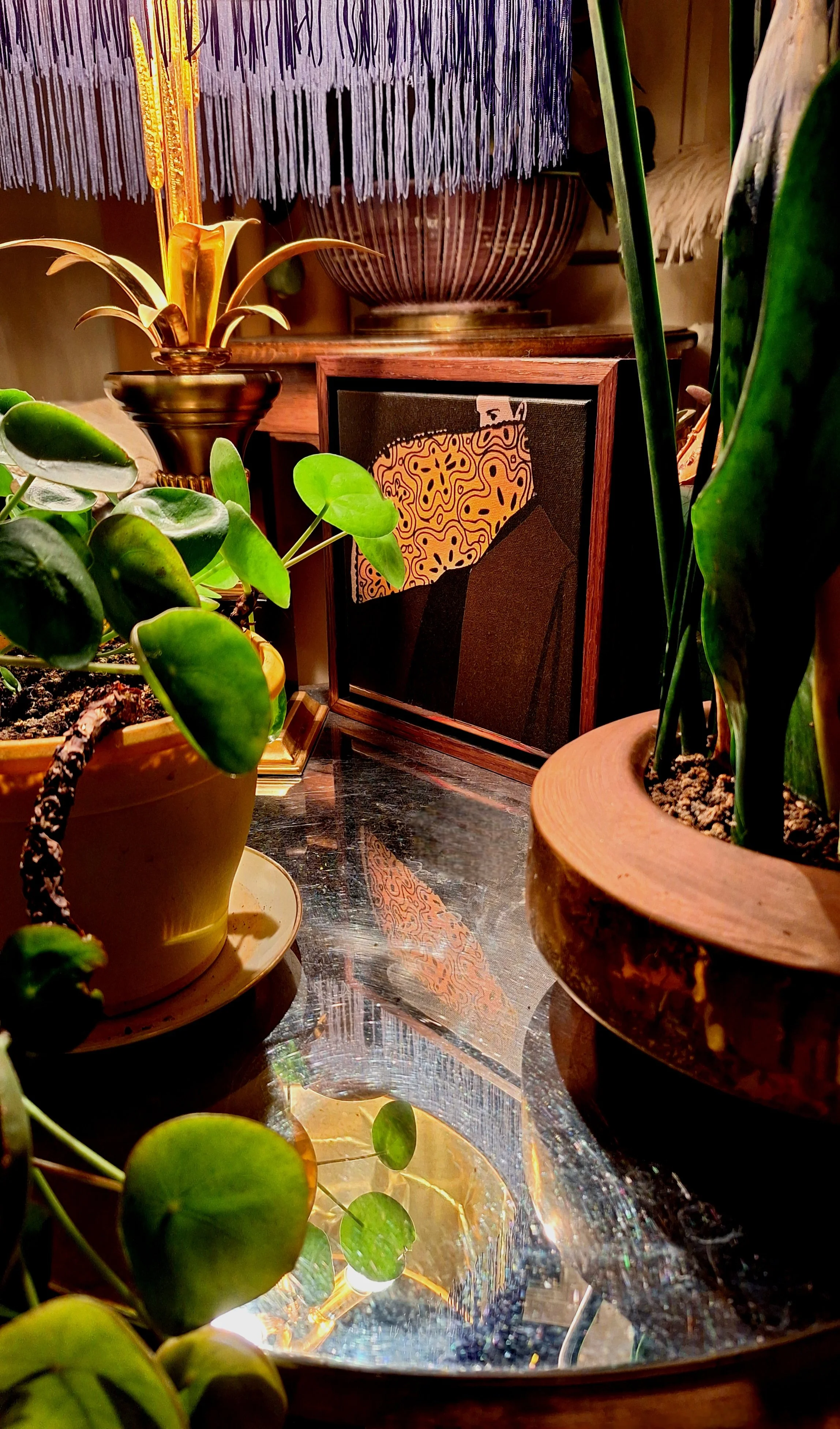 A collection of potted plants on a reflective surface, with decorative objects and artwork in the background.
