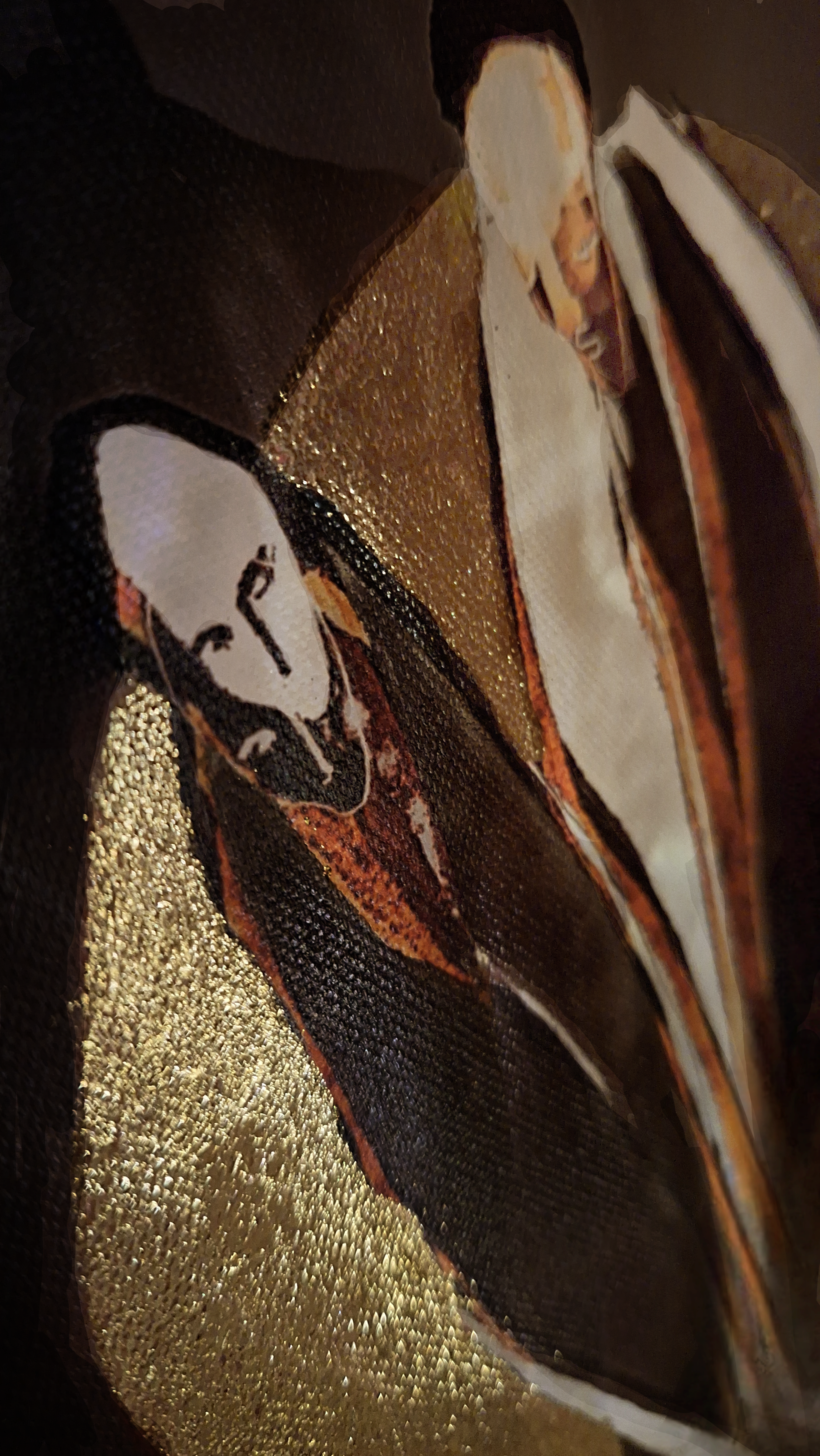 Close-up of a section of an artwork or fabric with black, white, and gold colors and a partial portrait of a person's face.