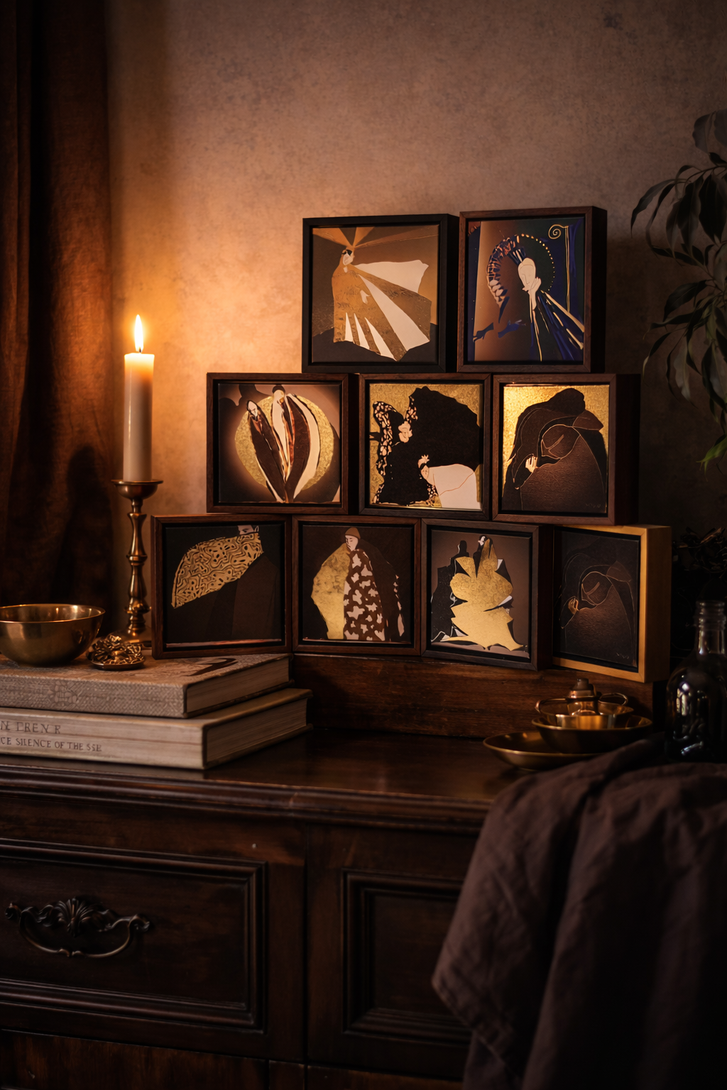A wooden table with a candle, a closed gold bowl, and a stack of books. Behind the table are nine framed abstract art prints arranged in a pyramid, illuminated by warm lighting.