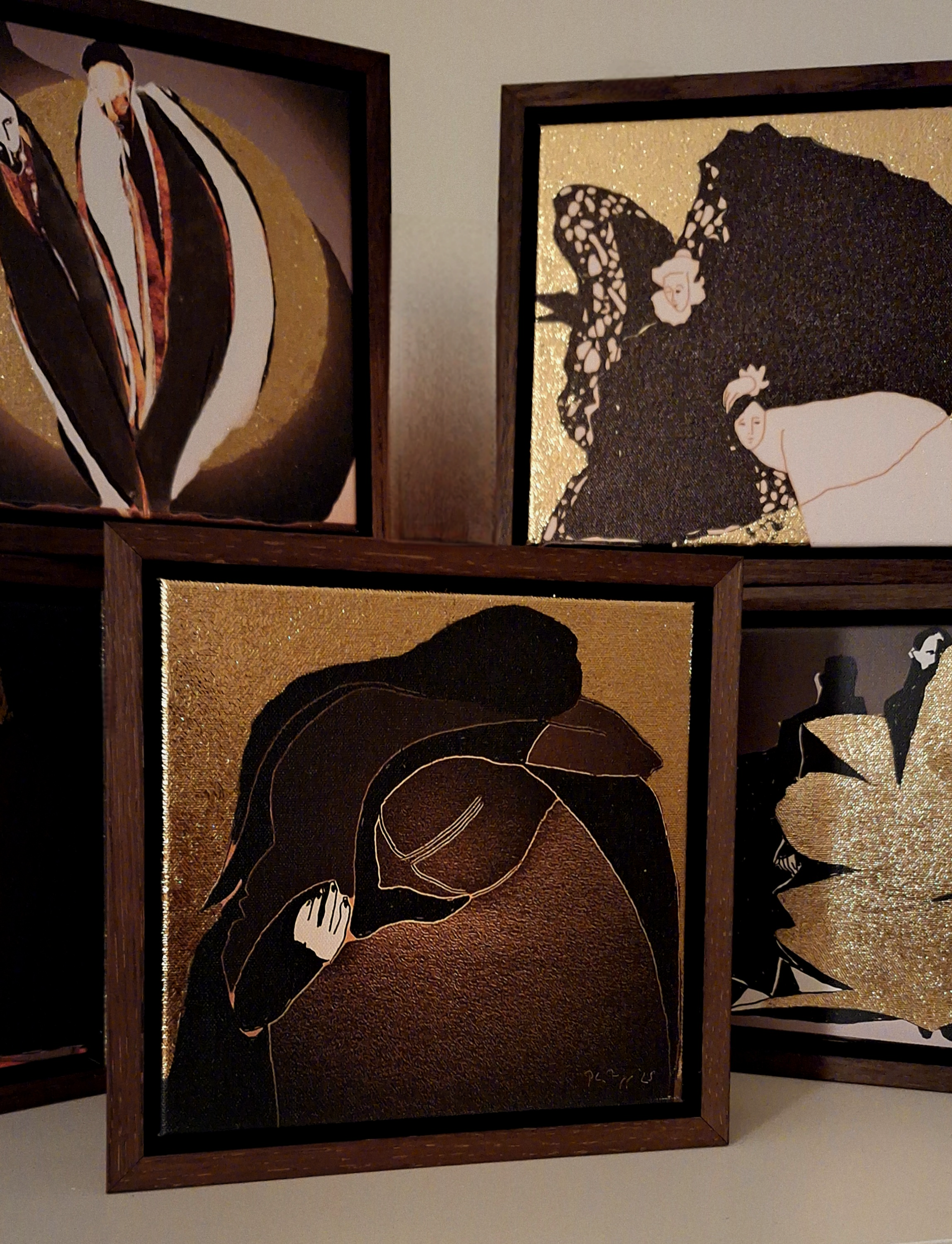 Four framed artwork pieces featuring abstract and stylized illustrations of women with dark hair, accented with gold backgrounds and detailing.