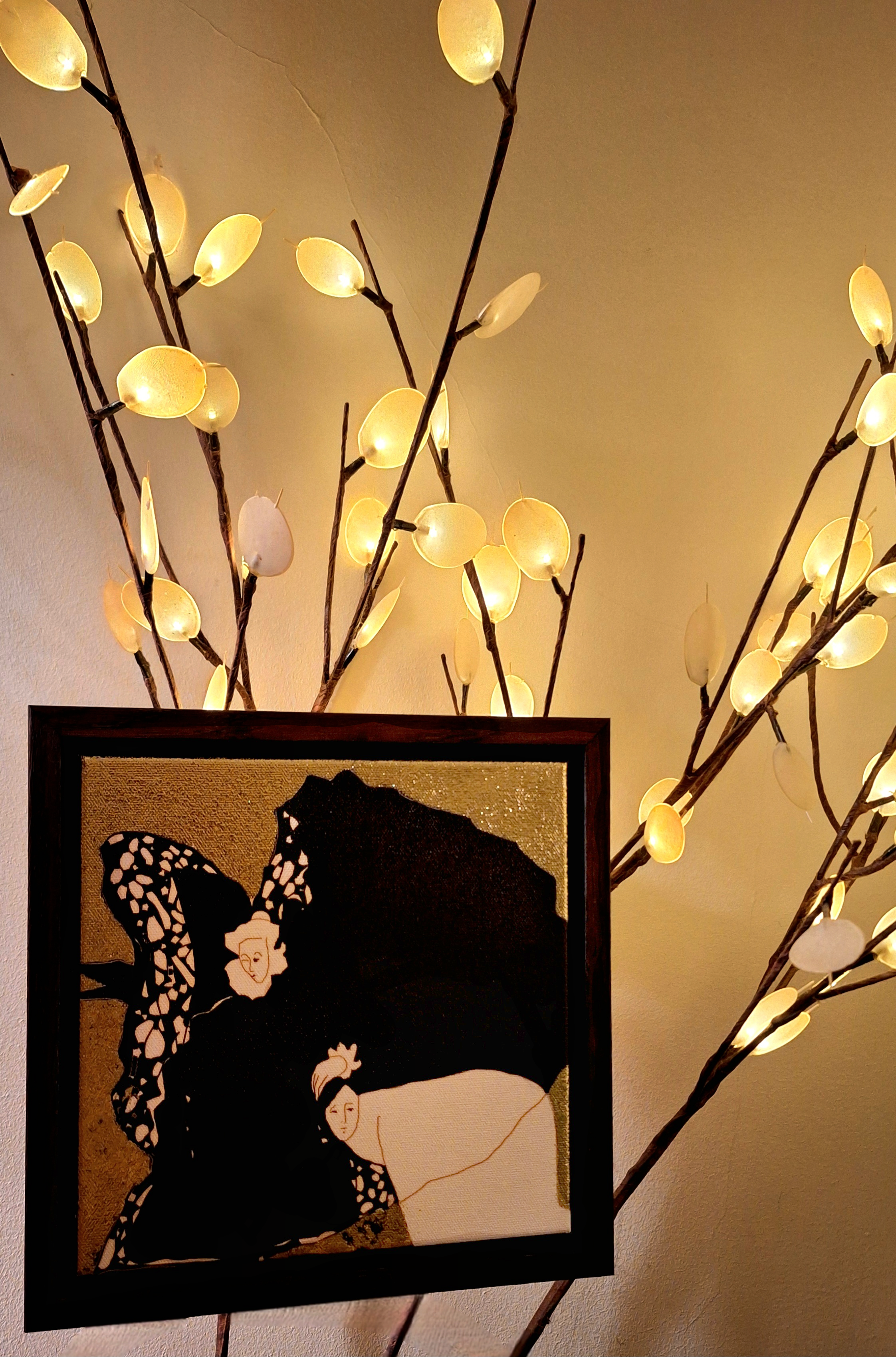 Decorative image featuring a framed artwork of two women with umbrellas and butterfly wings, surrounded by illuminated branch-like lights with oval-shaped bulbs.