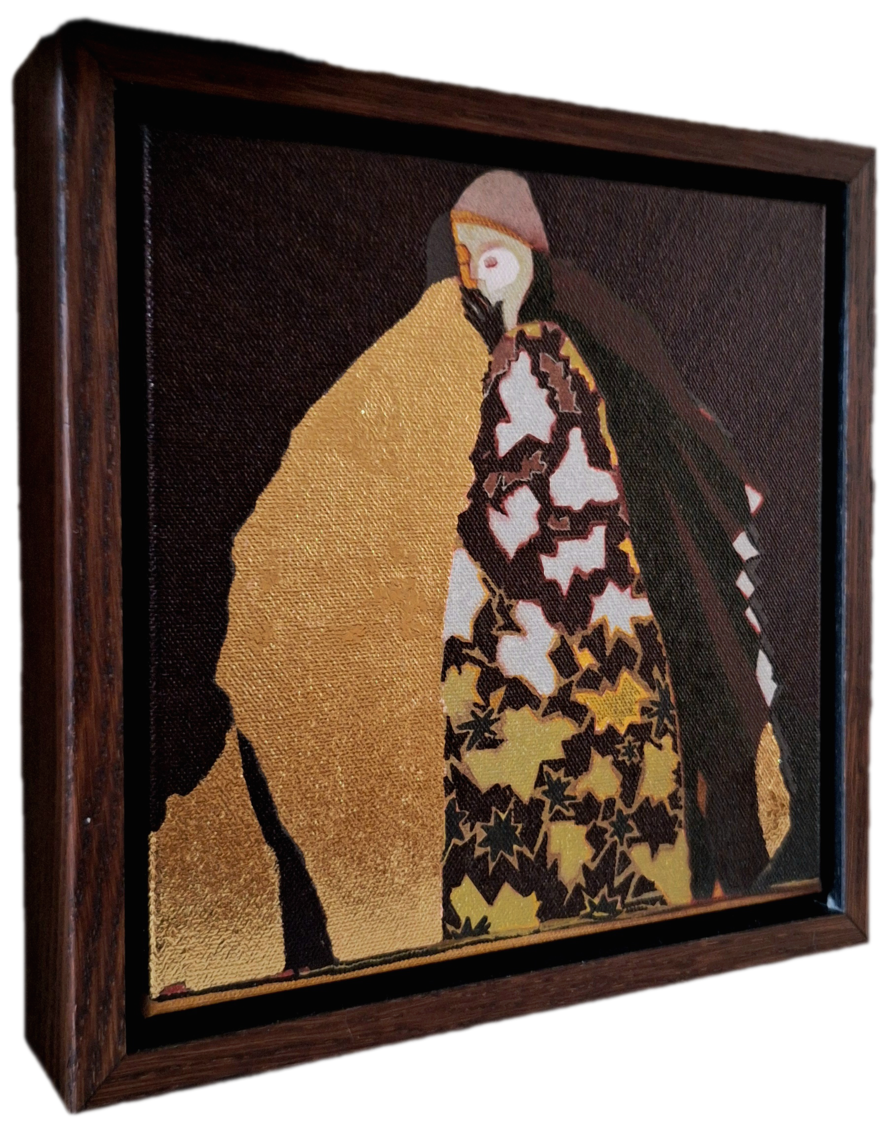 A framed embroidery artwork depicting a stylized woman with dark hair, wearing a pink hat, a yellow top, and a patterned cape with black stars, against a dark background.