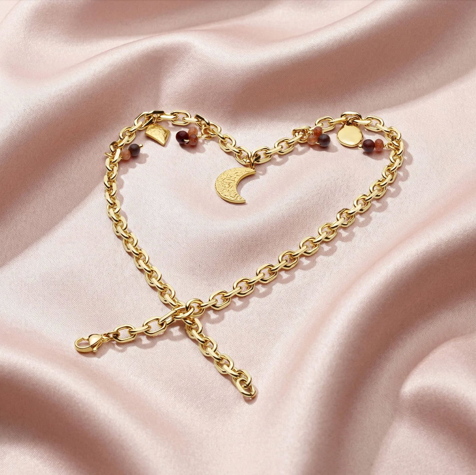 Premium styled packshot of gold chain with moon and gems on the background of pink cloth