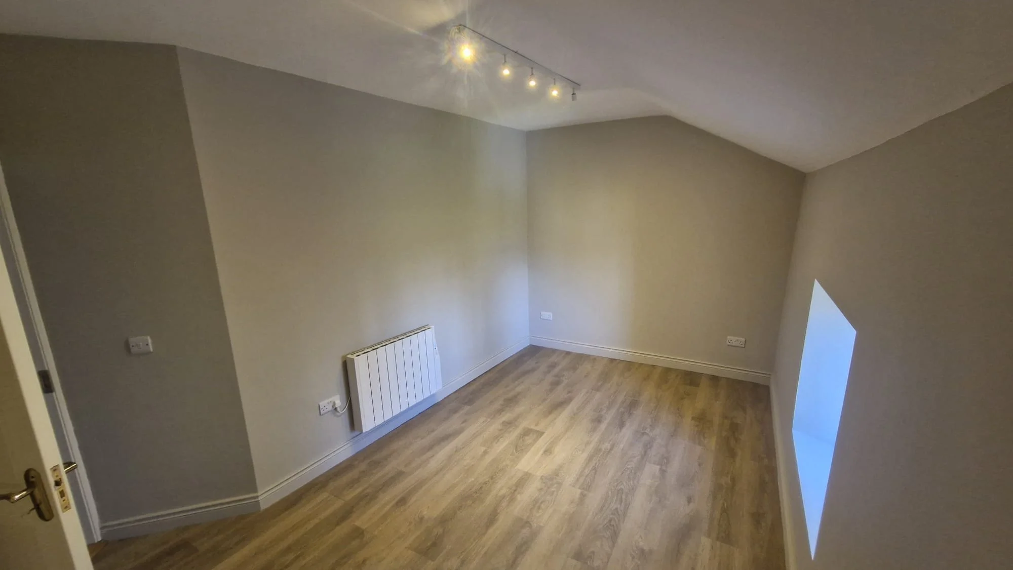Empty room with beige walls, wooden flooring, can be rented for professional use.