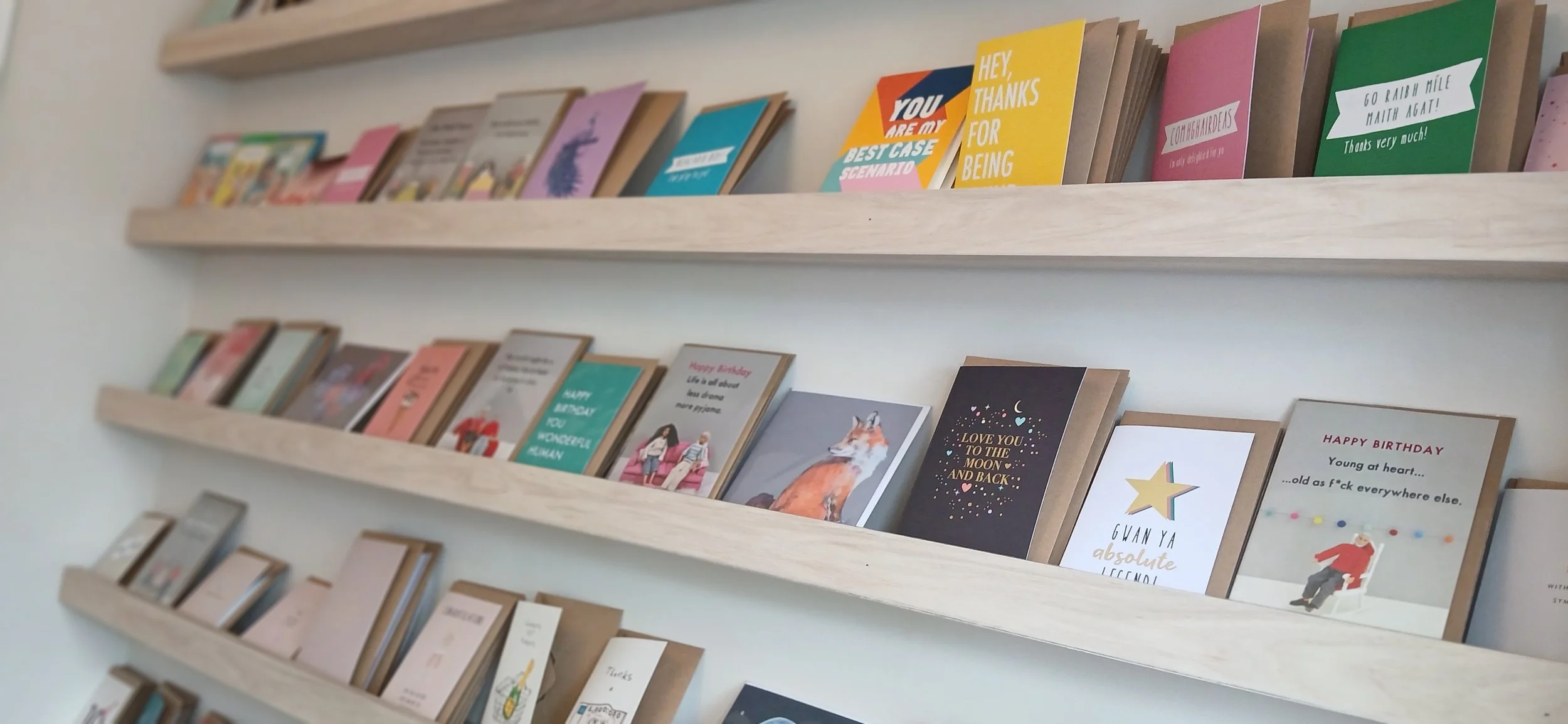 Display of greeting cards on wooden shelves, with various colorful designs and messages.