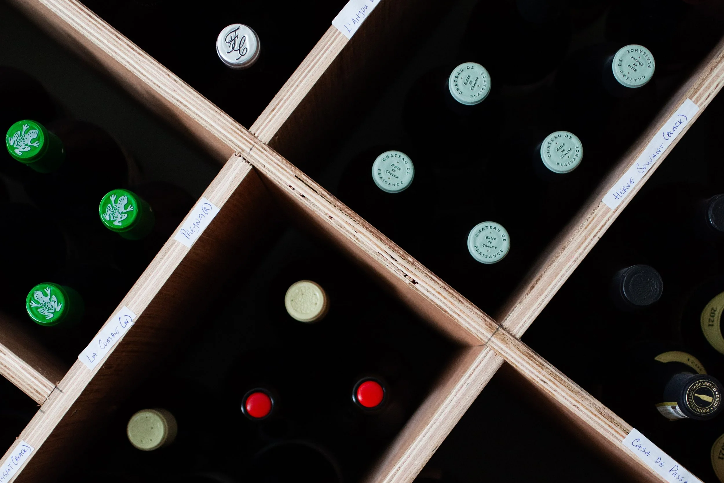 Shelf with wine bottles divided into sections labeled with handwritten notes.