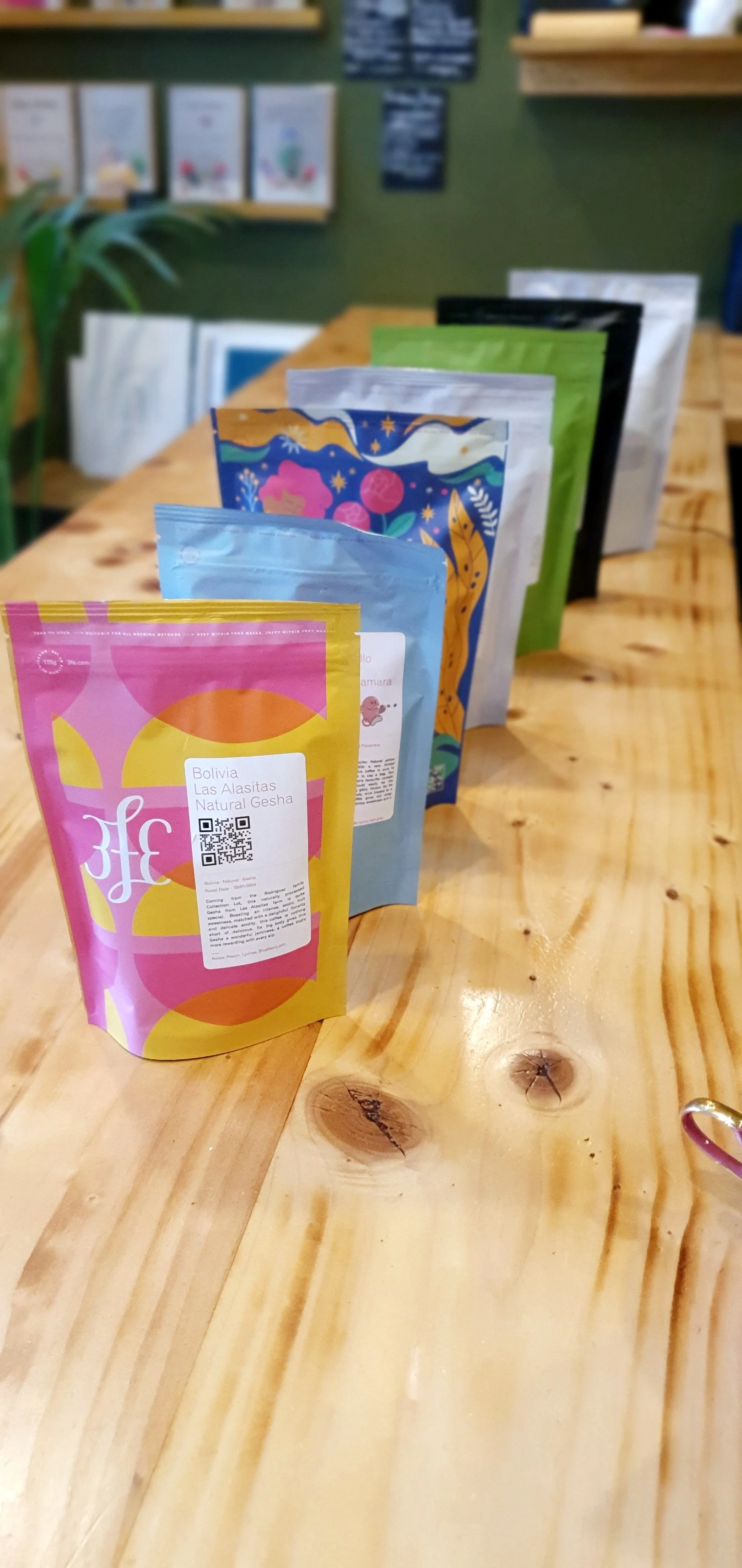 Several colorful packages of tea or coffee lined up on a wooden table in a store or cafe.