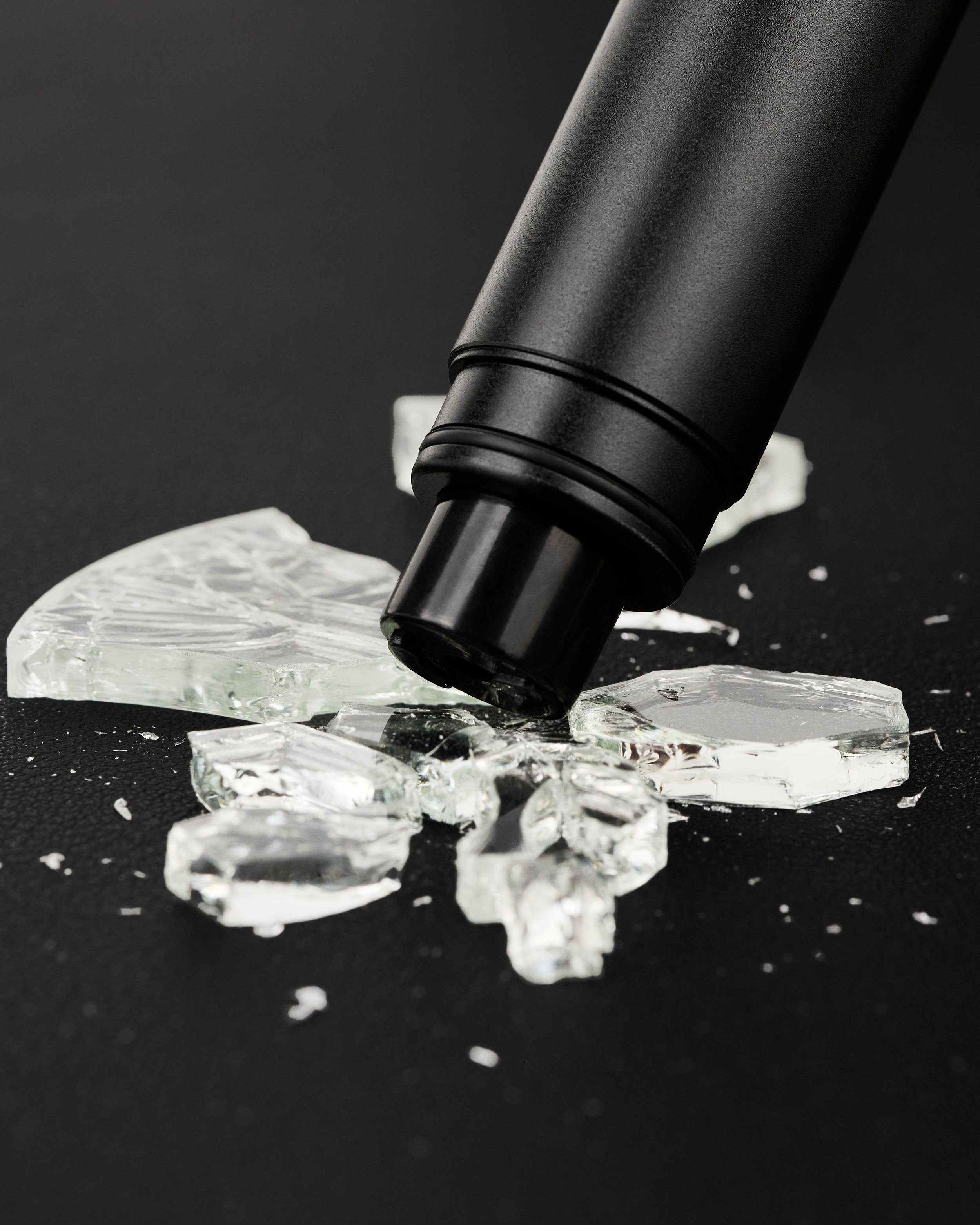 martelo de segurança de carro preto sobre pedaços de vidro quebrado em uma superfície preta.
black car safety hammer on pieces of broken glass on a black surface.