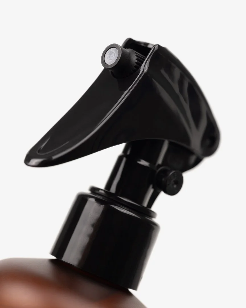Close-up of a black spray nozzle attached to a pump dispenser, positioned at an angle against a plain white background.