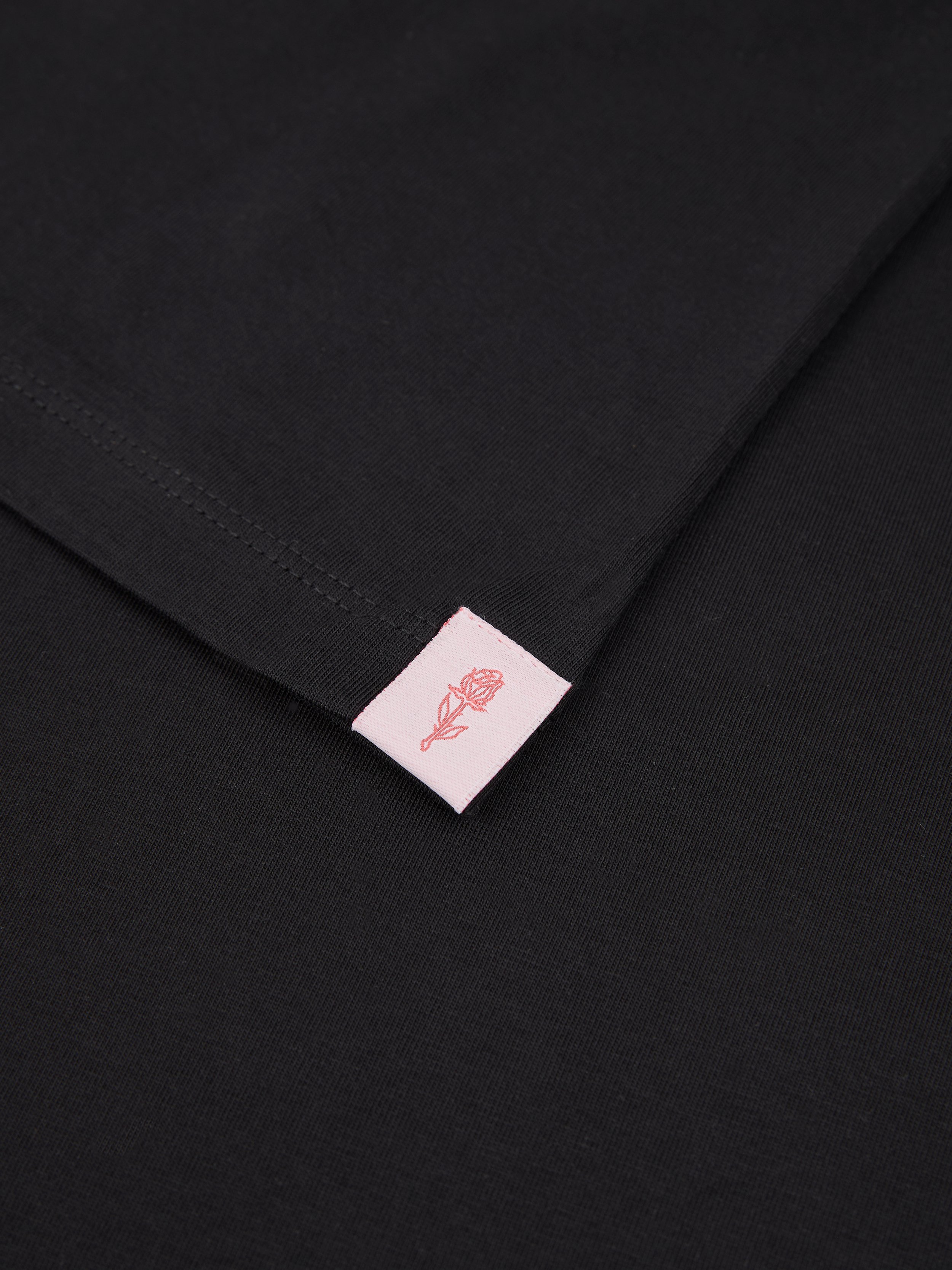Close-up of a black fabric with a pink tag featuring a rose illustration.