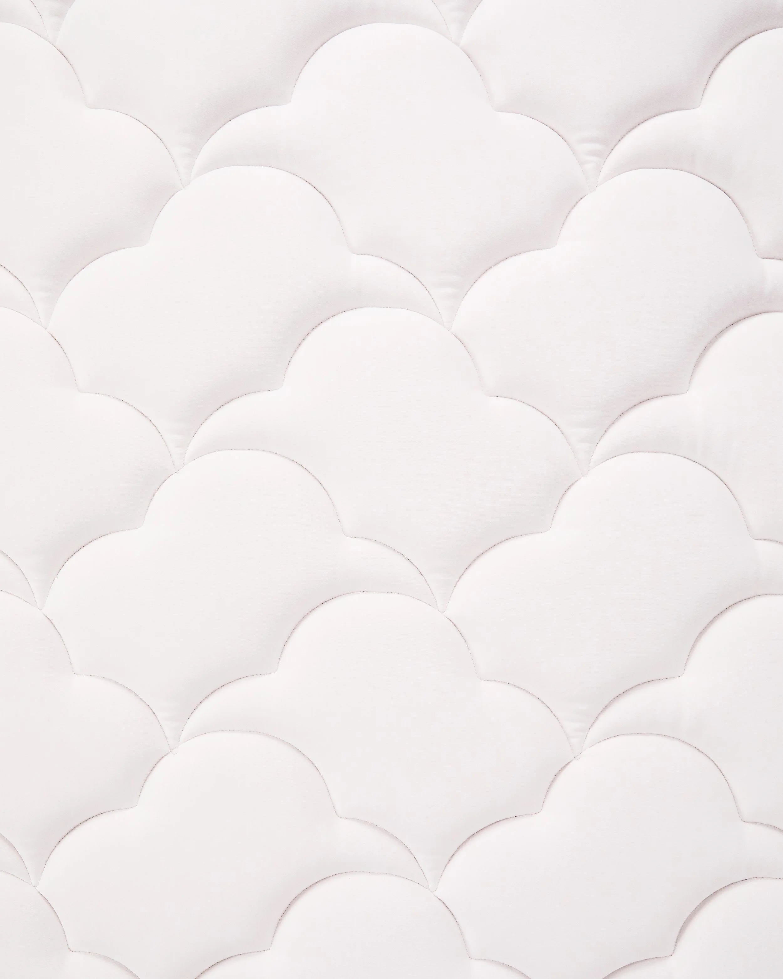 Close-up of a white quilted or padded surface with overlapping scalloped patterns.