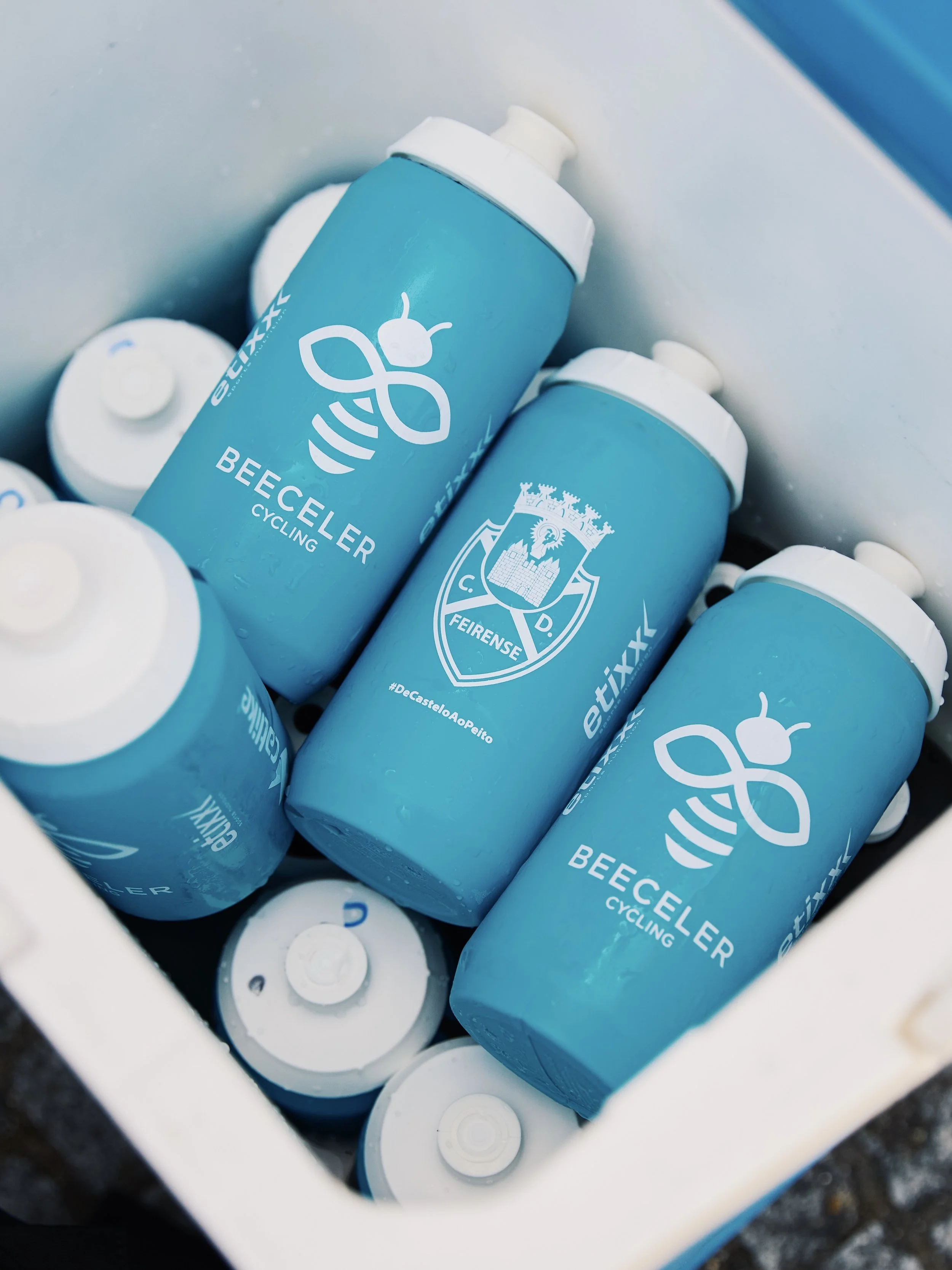 Multiple blue bottles labeled 'Beeceler Cycling' with a bee and a crest logo inside a white cooler.