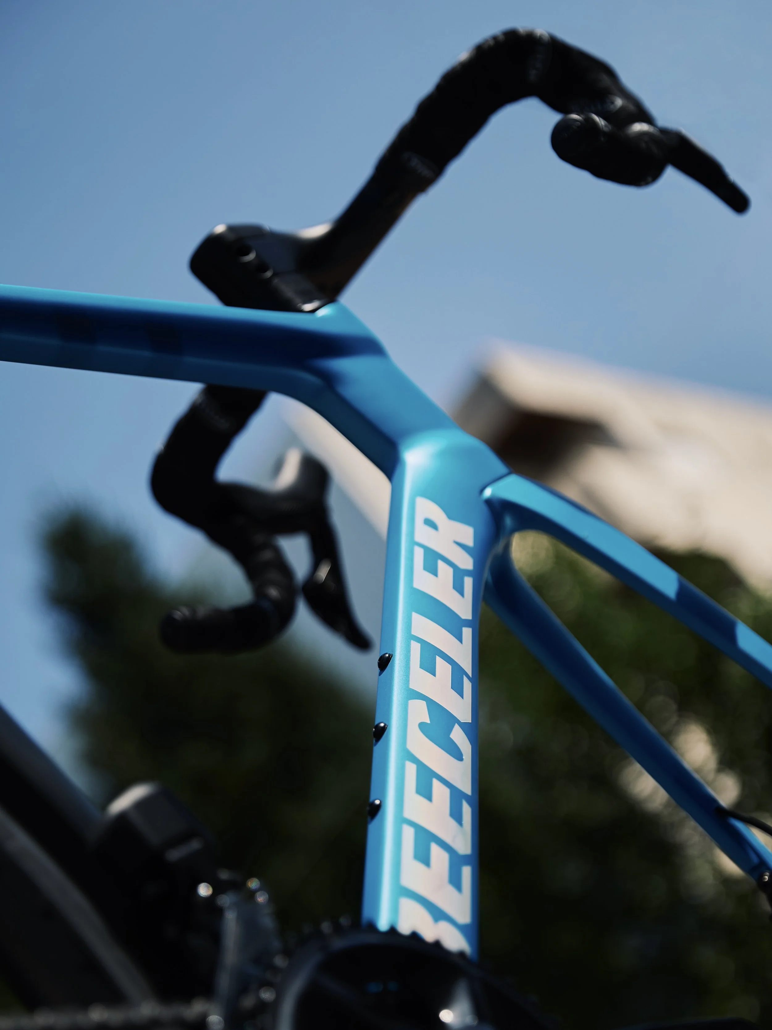 Close-up of a blue bicycle frame with Black handlebars and the word "SEELEY" written on it, against a background of a partly cloudy sky and trees.