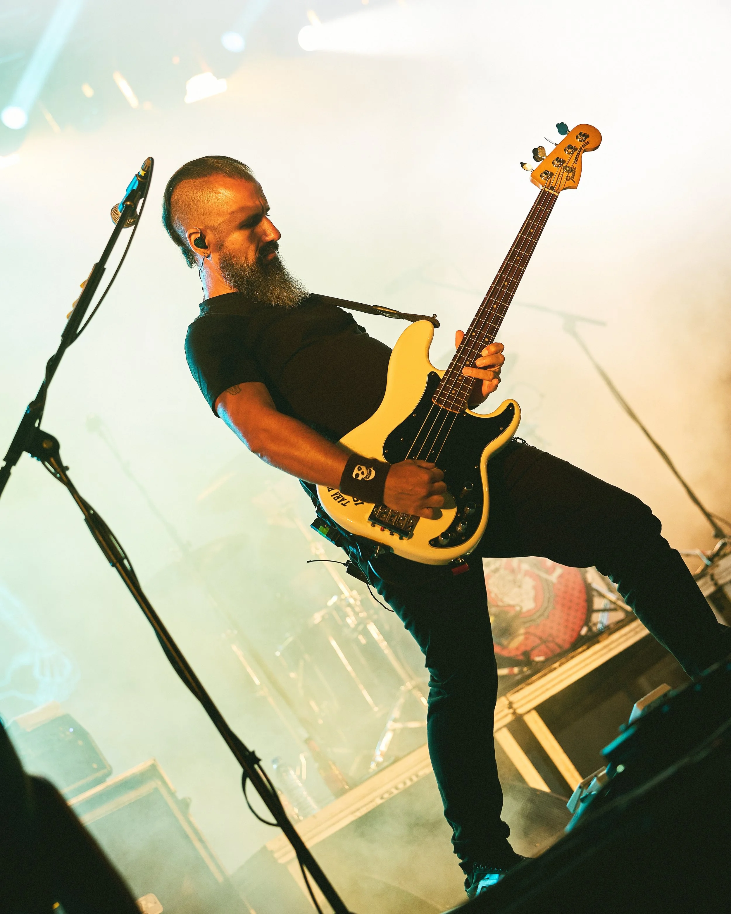 Male guitarist playing an electric bass guitar on stage during a concert.