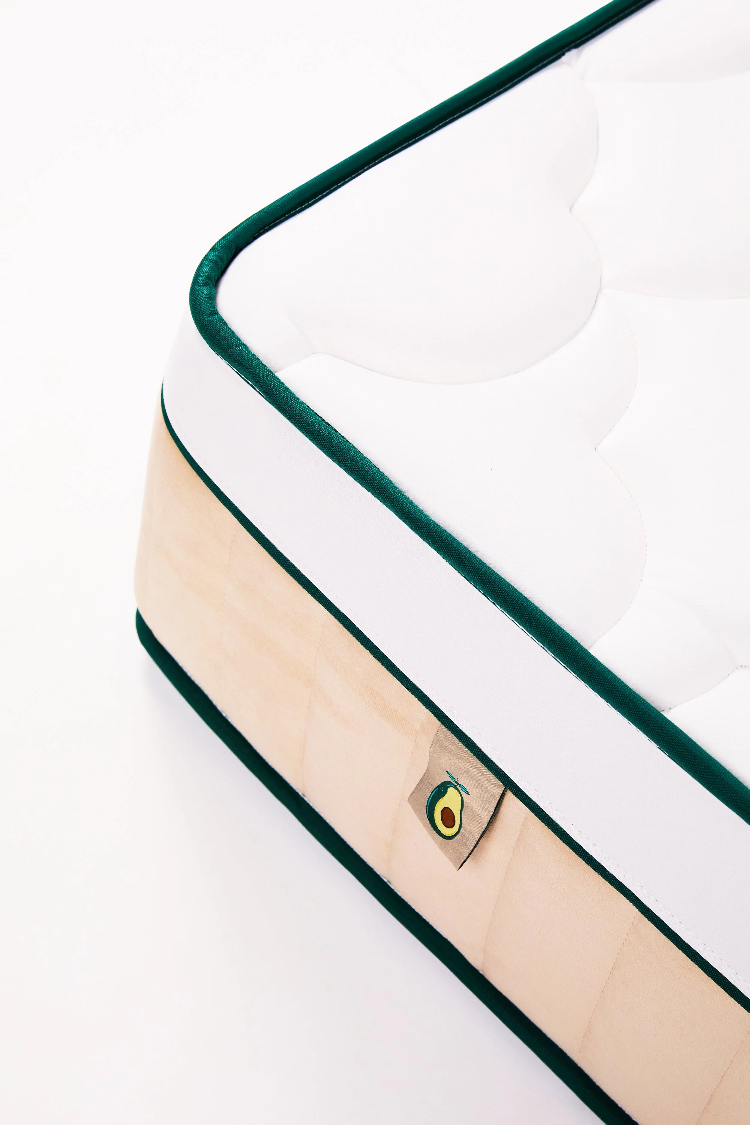 Close-up of a mattress with white quilting, green piping, and a beige fabric panel with an avocado logo on the side.