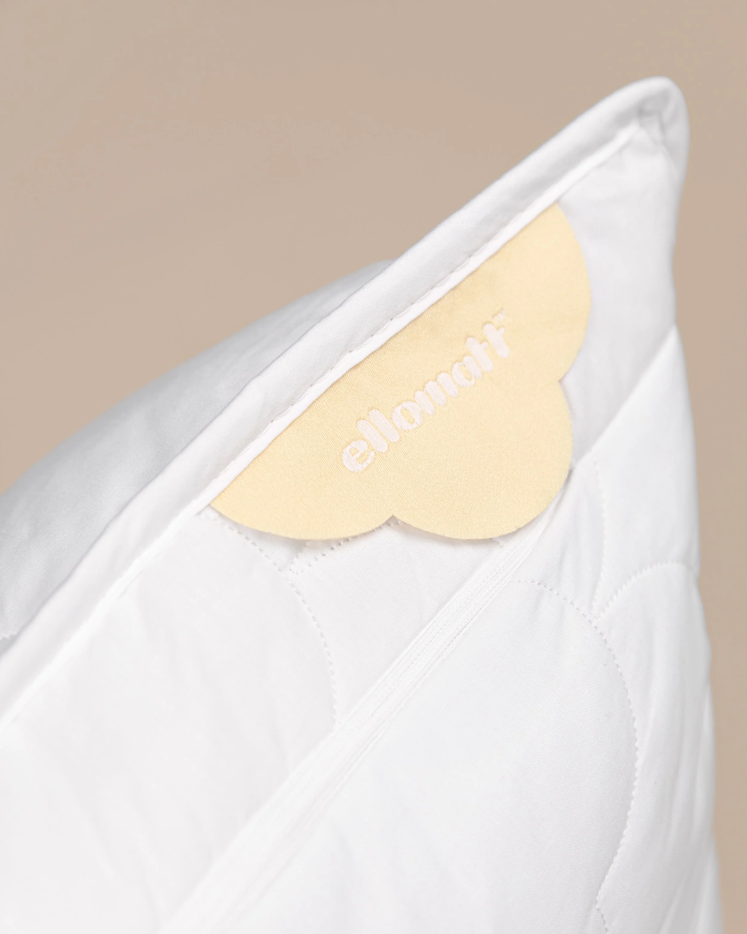 A close-up of a white pillow with a yellow cloud-shaped tag that has the word 'elomonair' embroidered in white.