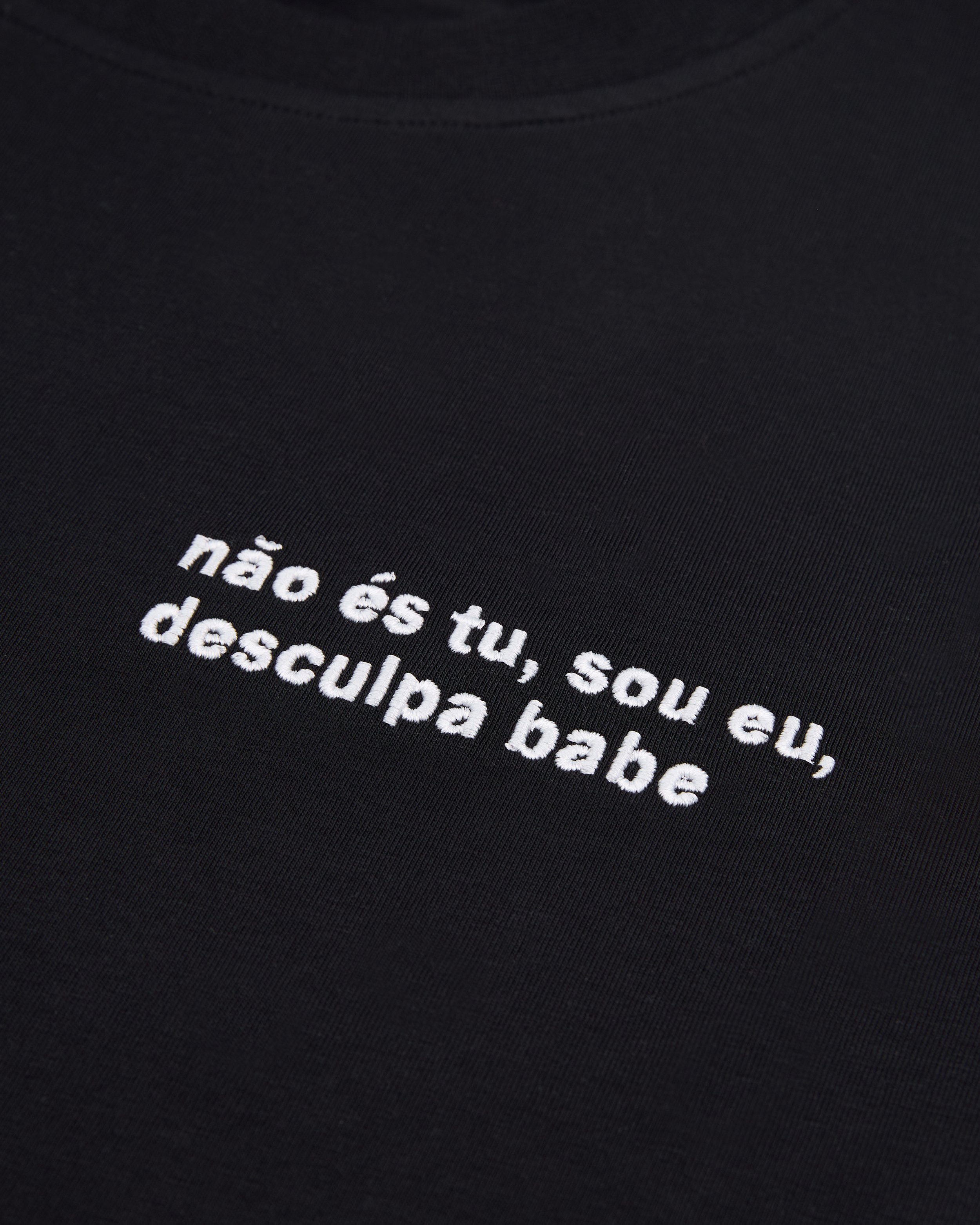 Close-up of black fabric with white embroidered text in Portuguese.