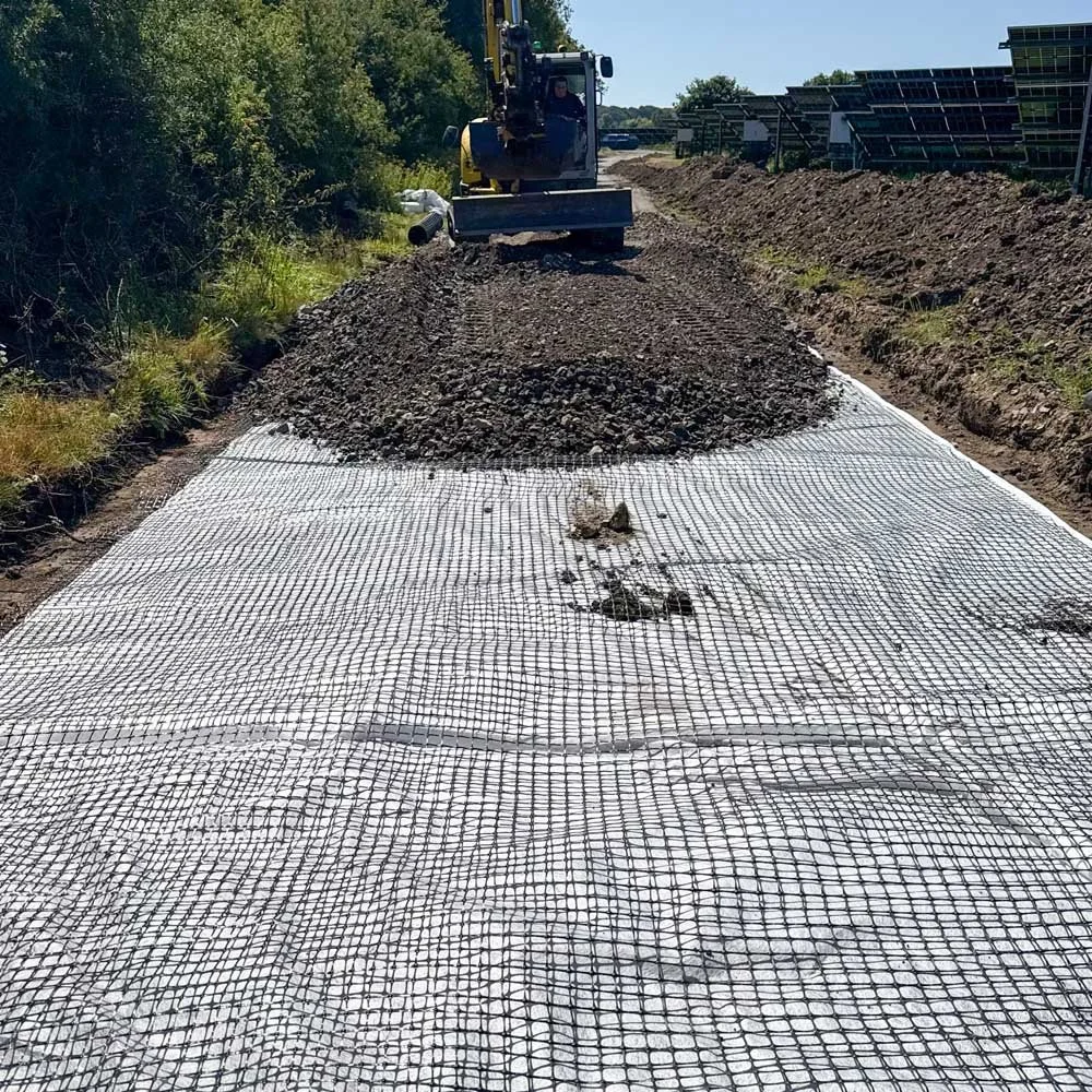 Construction site with a yellow bulldozer spreading gravel on a road surface covered with a white geotextile fabric.