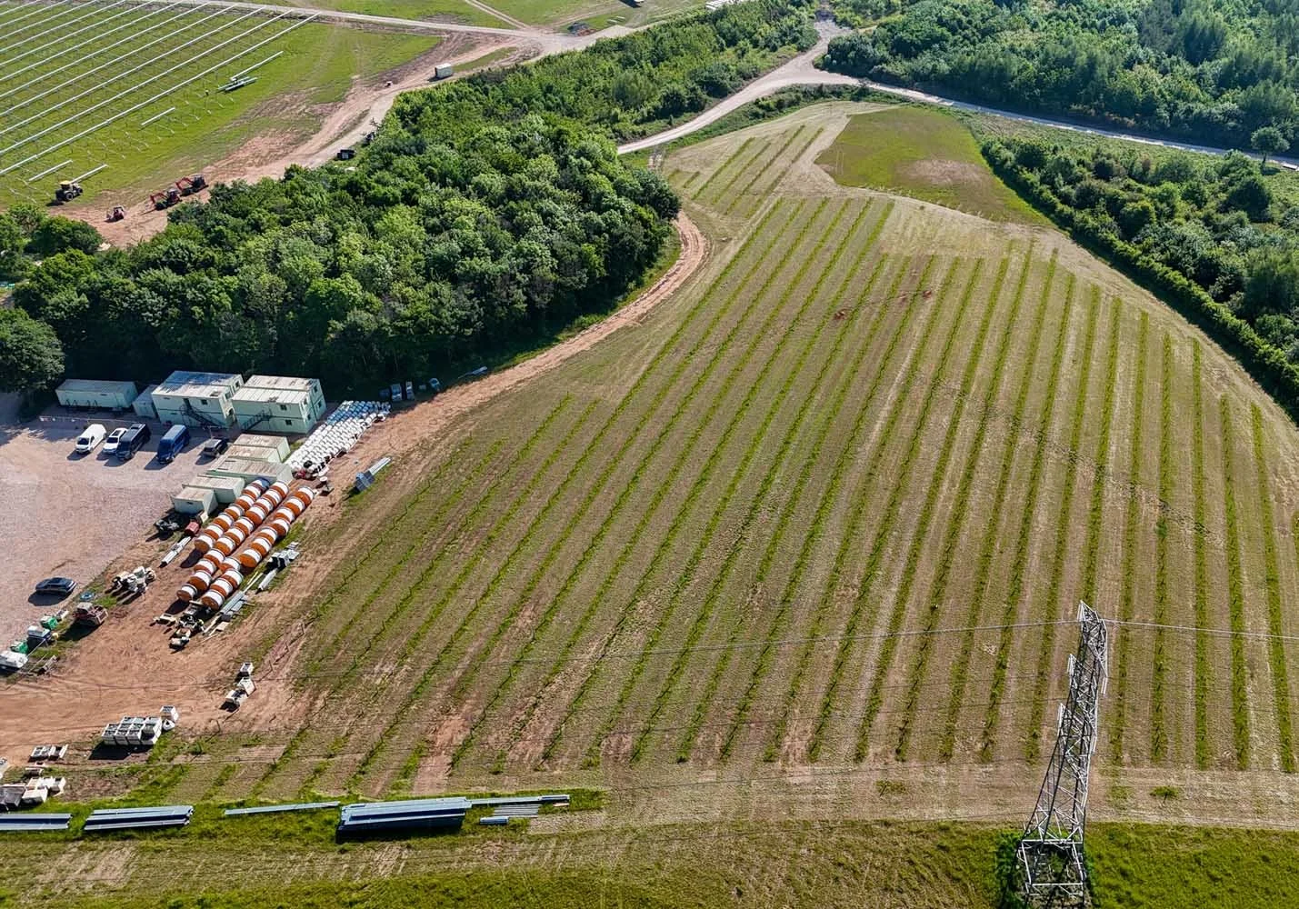 Aerial view of a farm with fields, trees, construction equipment, and a power line tower.