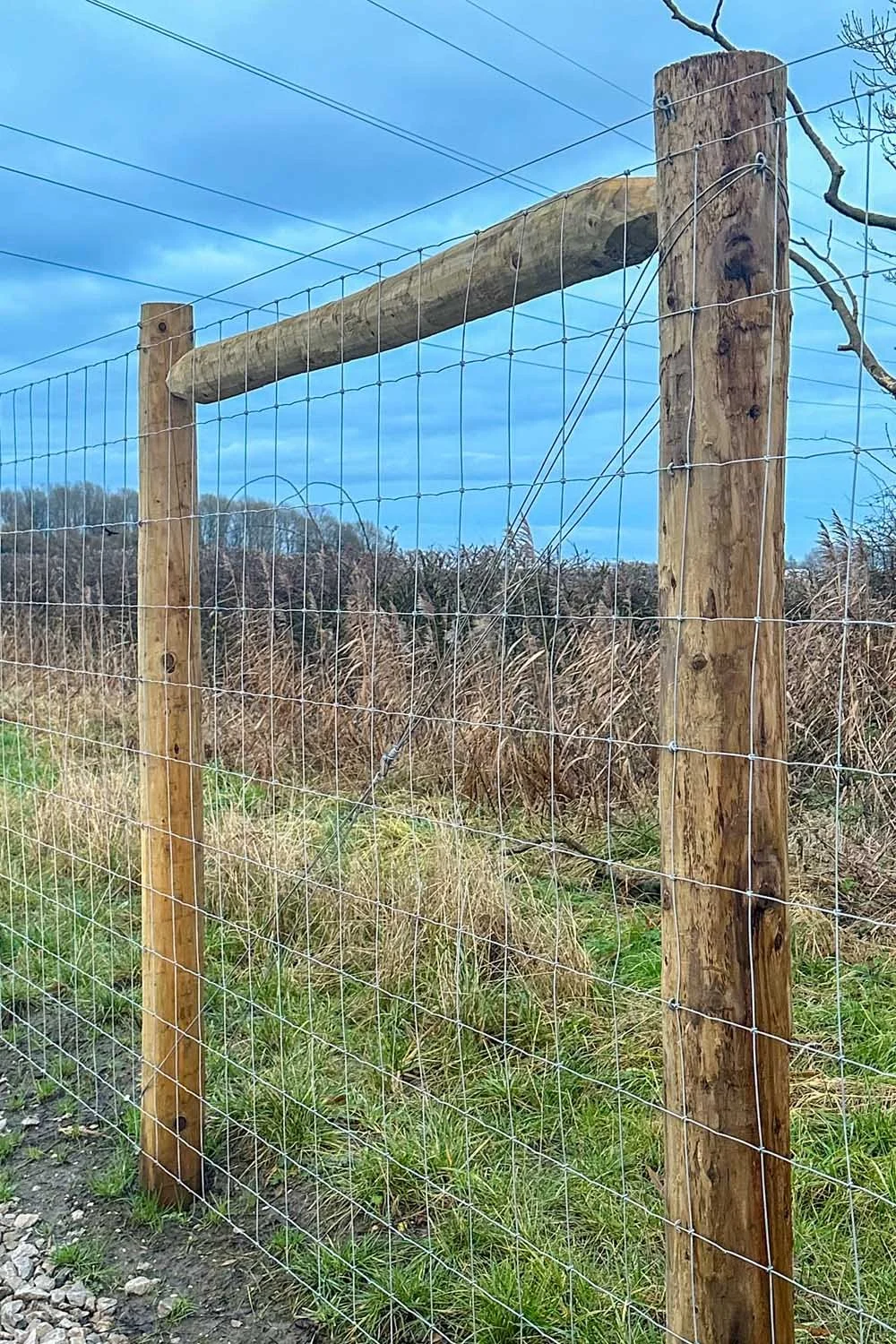 Wooden fence with wire mesh panels in a grassy field under a cloudy blue sky.