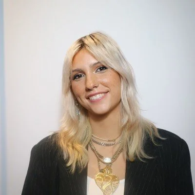 Portrait of a young woman with blonde hair and layered necklaces.