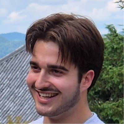 Portrait of a young man with brown hair outdoors.