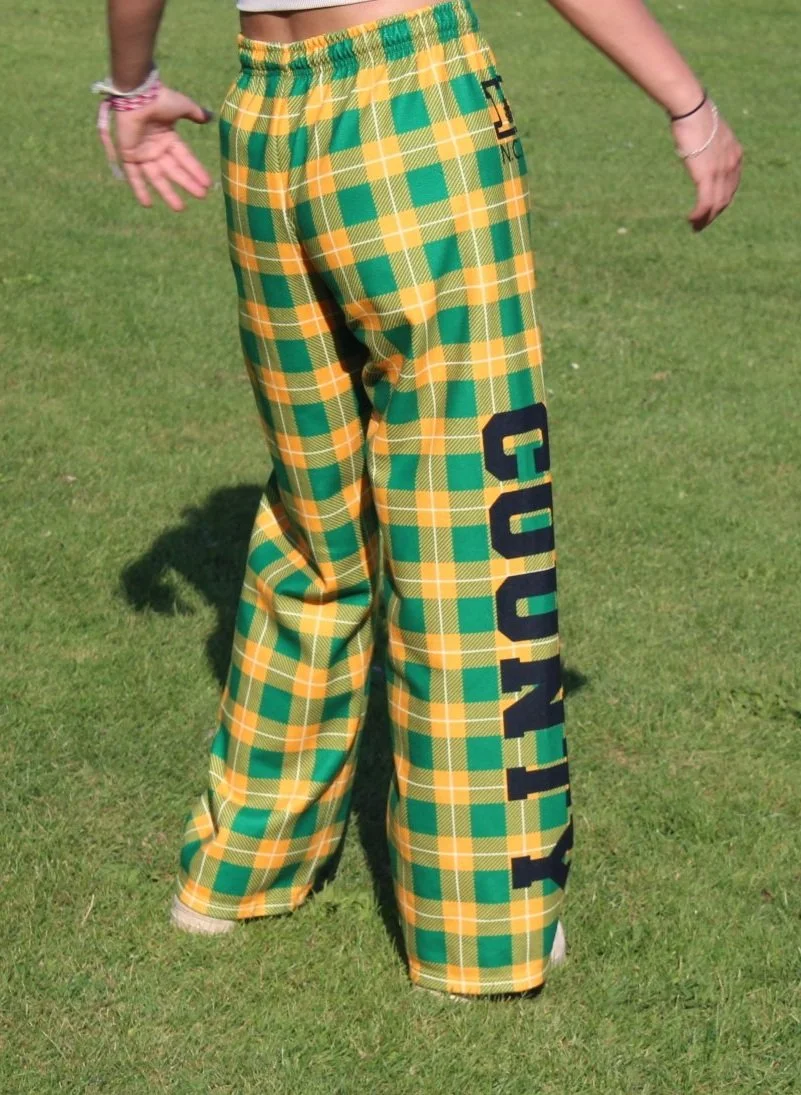 Person standing on grass wearing yellow and green plaid pants with the word "LOYALTY" printed on the leg.