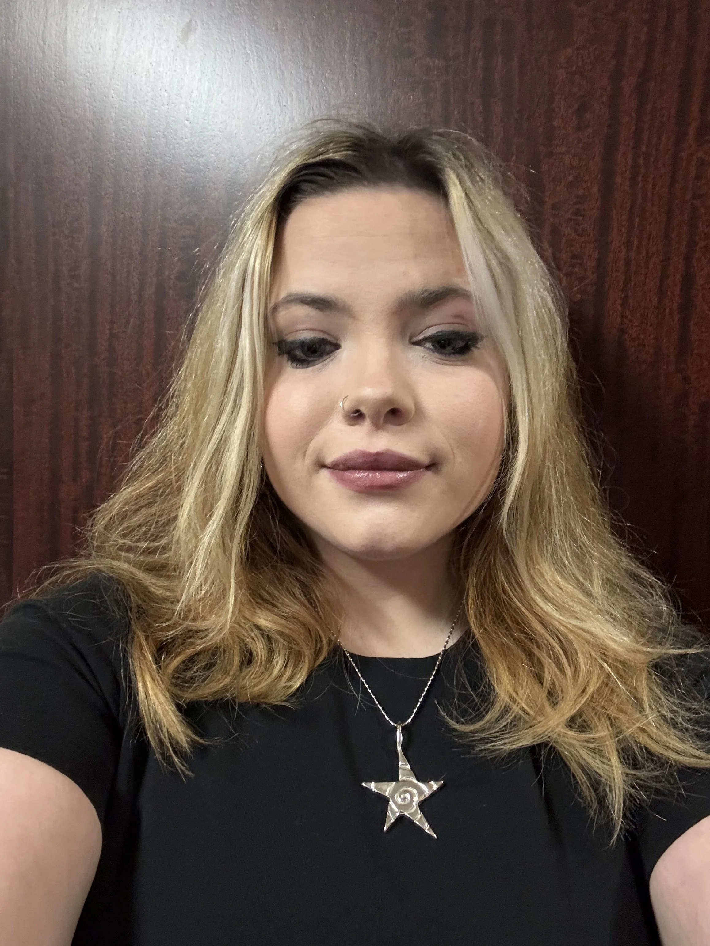 Close-up of a woman with blonde hair wearing a black shirt and a star-shaped pendant necklace.