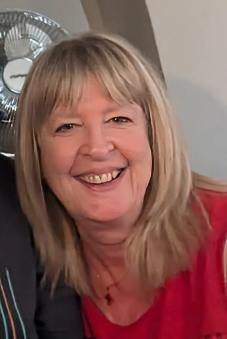 Home-Start trustee, A smiling woman with blonde hair and bangs, wearing a red top, in an indoor setting.