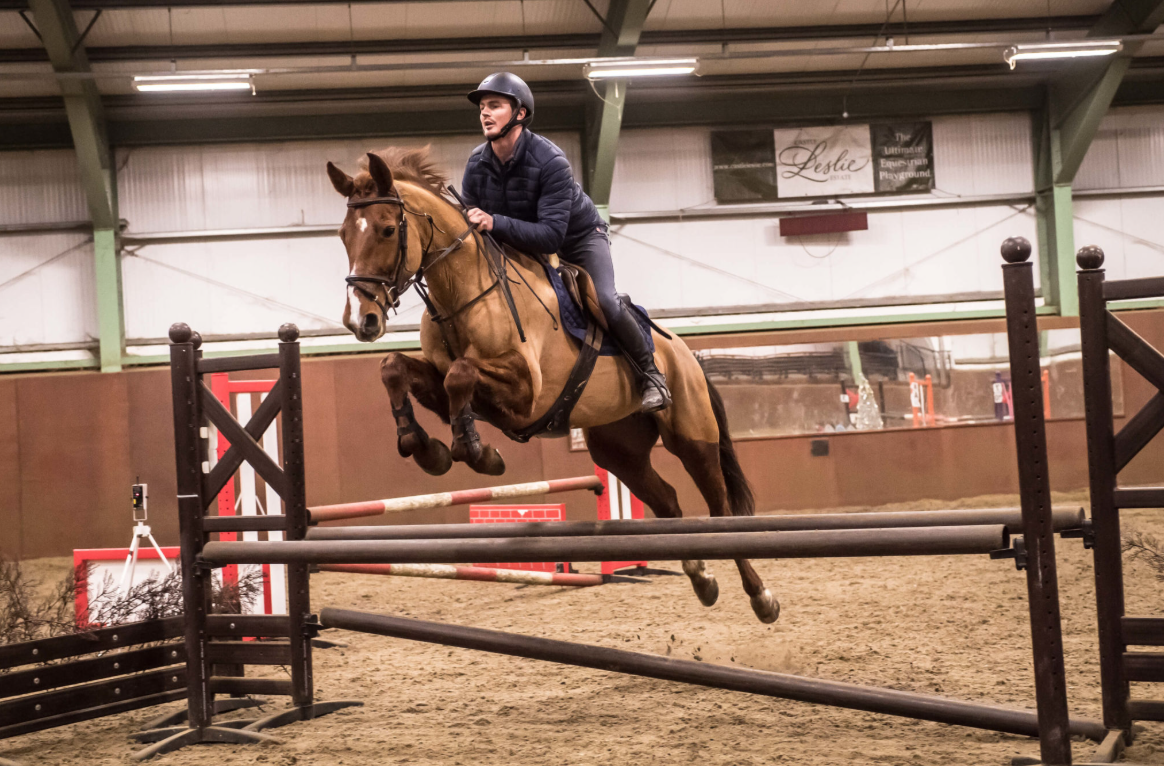 A person riding a horse during an indoor equestrian jumping event, jumping over a hurdle.