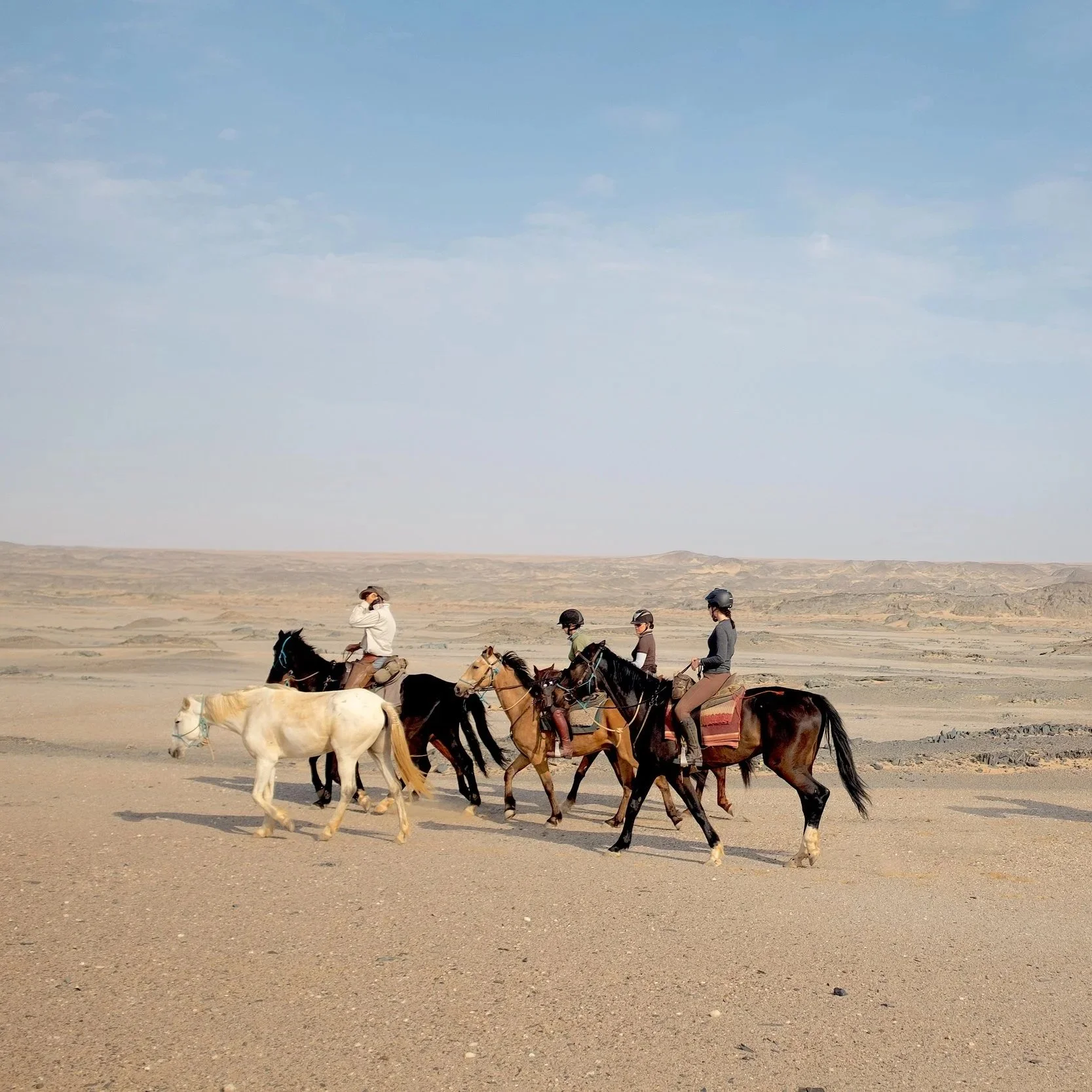 Five people riding horses in a desert landscape under a blue sky.