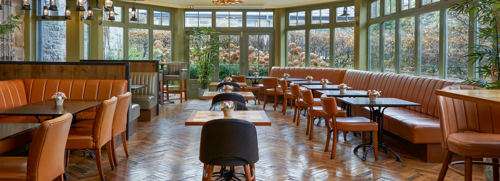 Interior of a restaurant with large windows, brown leather chairs, and tables decorated with small flower arrangements.