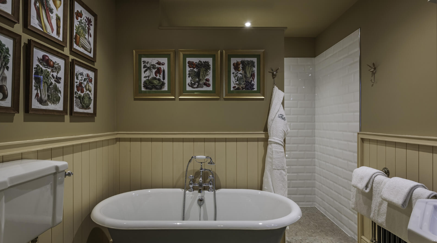 Bathroom featuring a vintage bathtub, framed botanical prints on the walls, a white tiled shower area, and white towels.