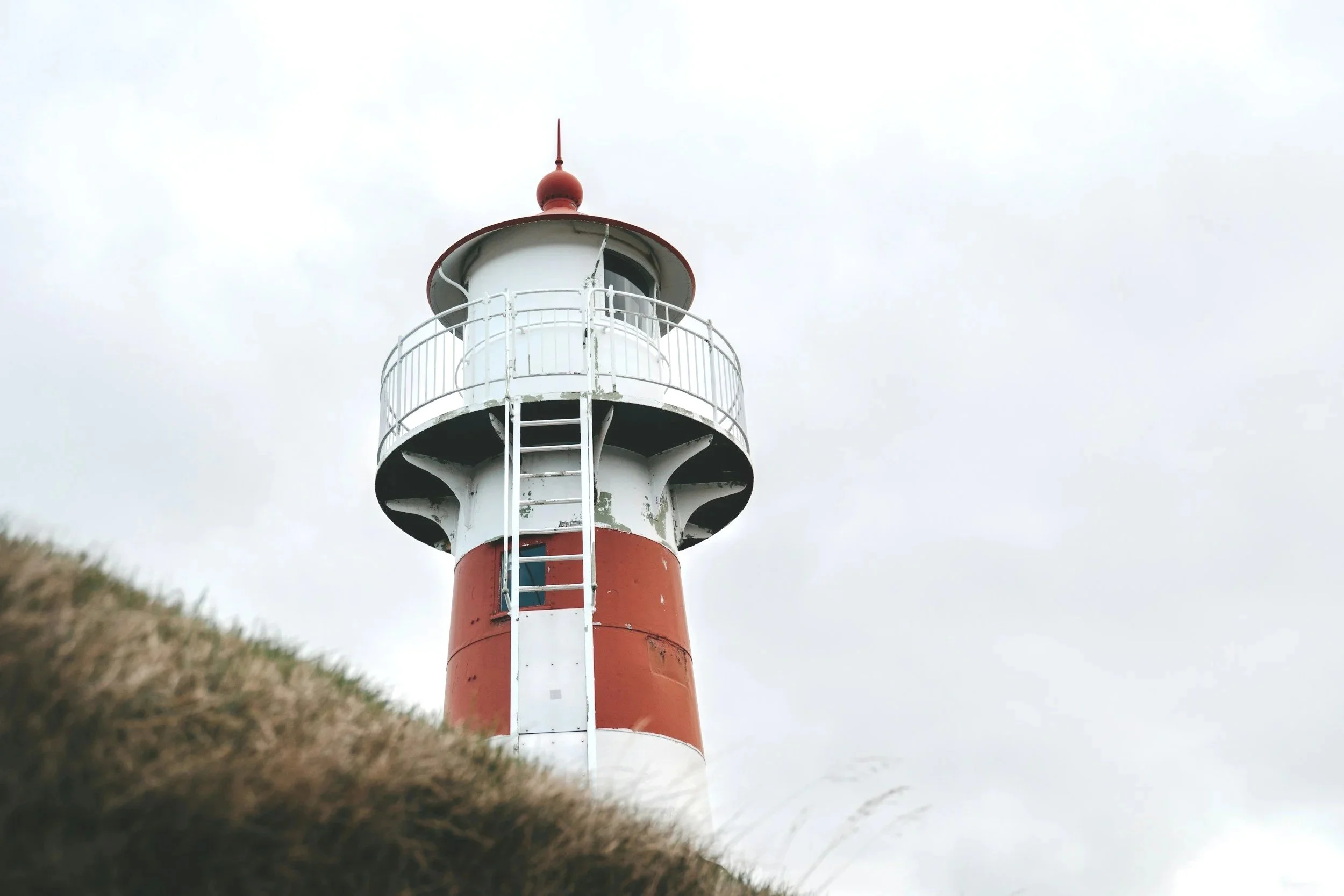 A red and white striped lighthouse on a grassy hill under a cloudy sky.