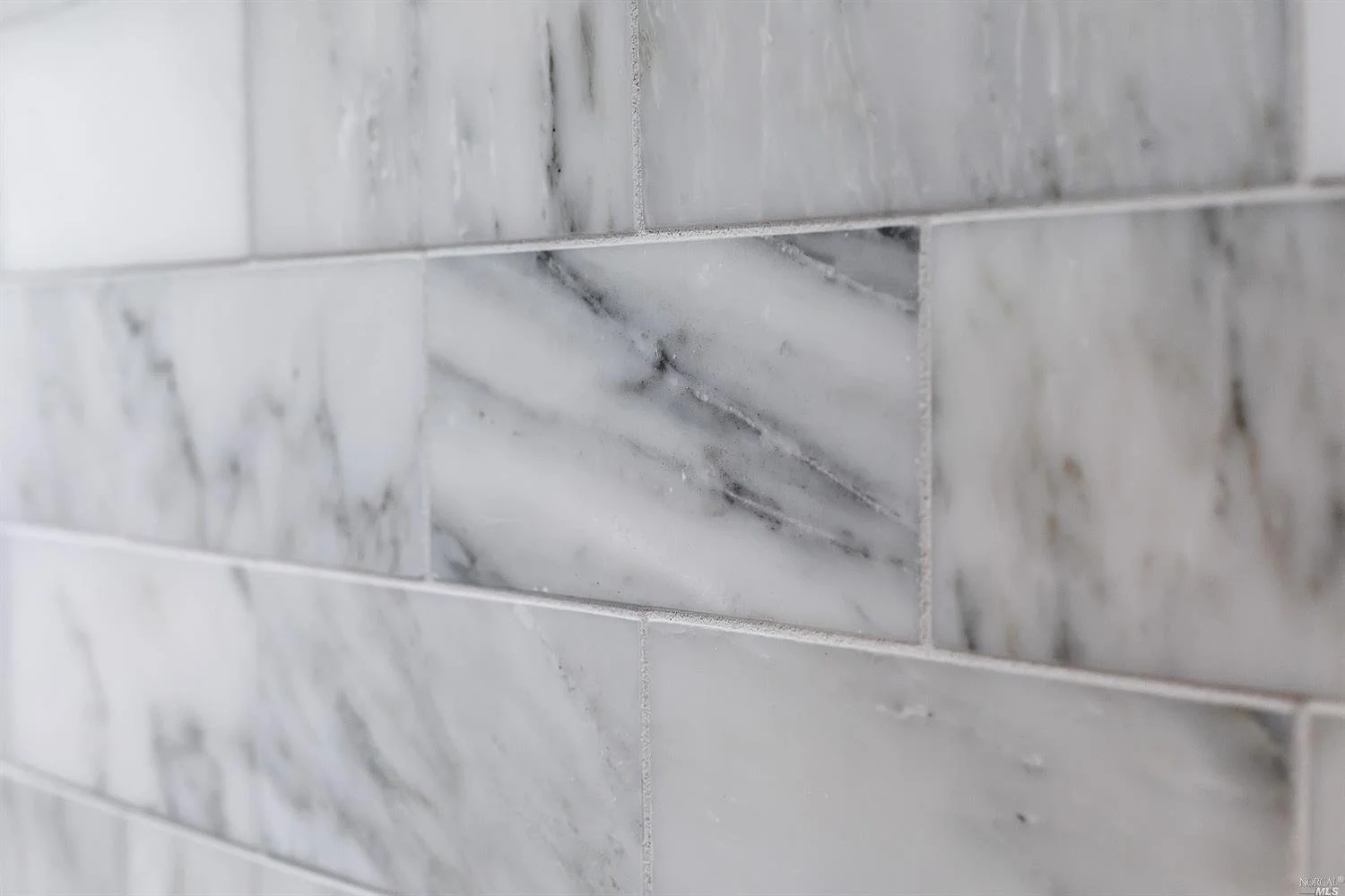 Close-up of a wall with light gray marble tiles, including one decorative rectangular marble accent tile.