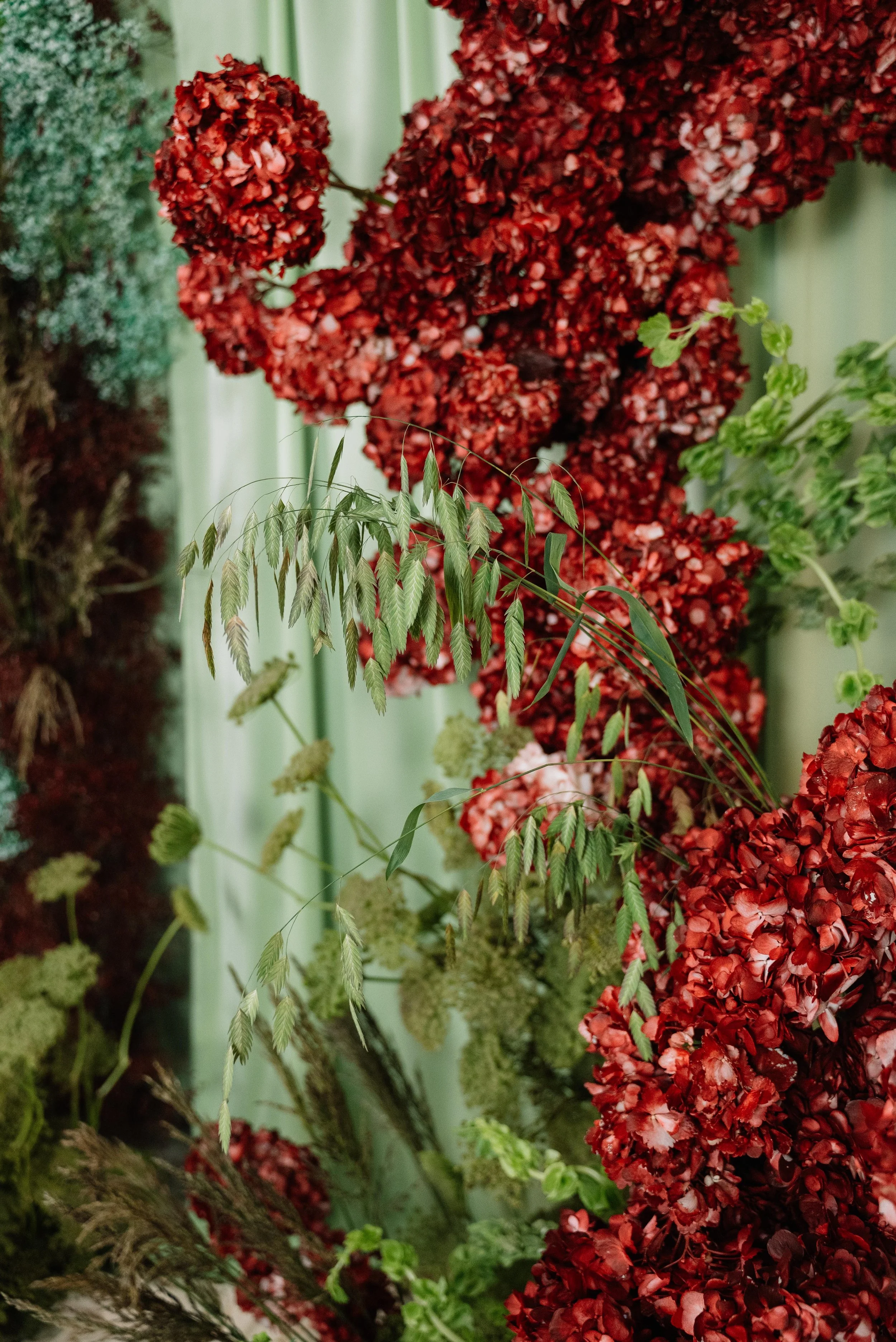 Variedad de flores y plantas decorativas con tonos rojos y verdes en un arreglo floral.