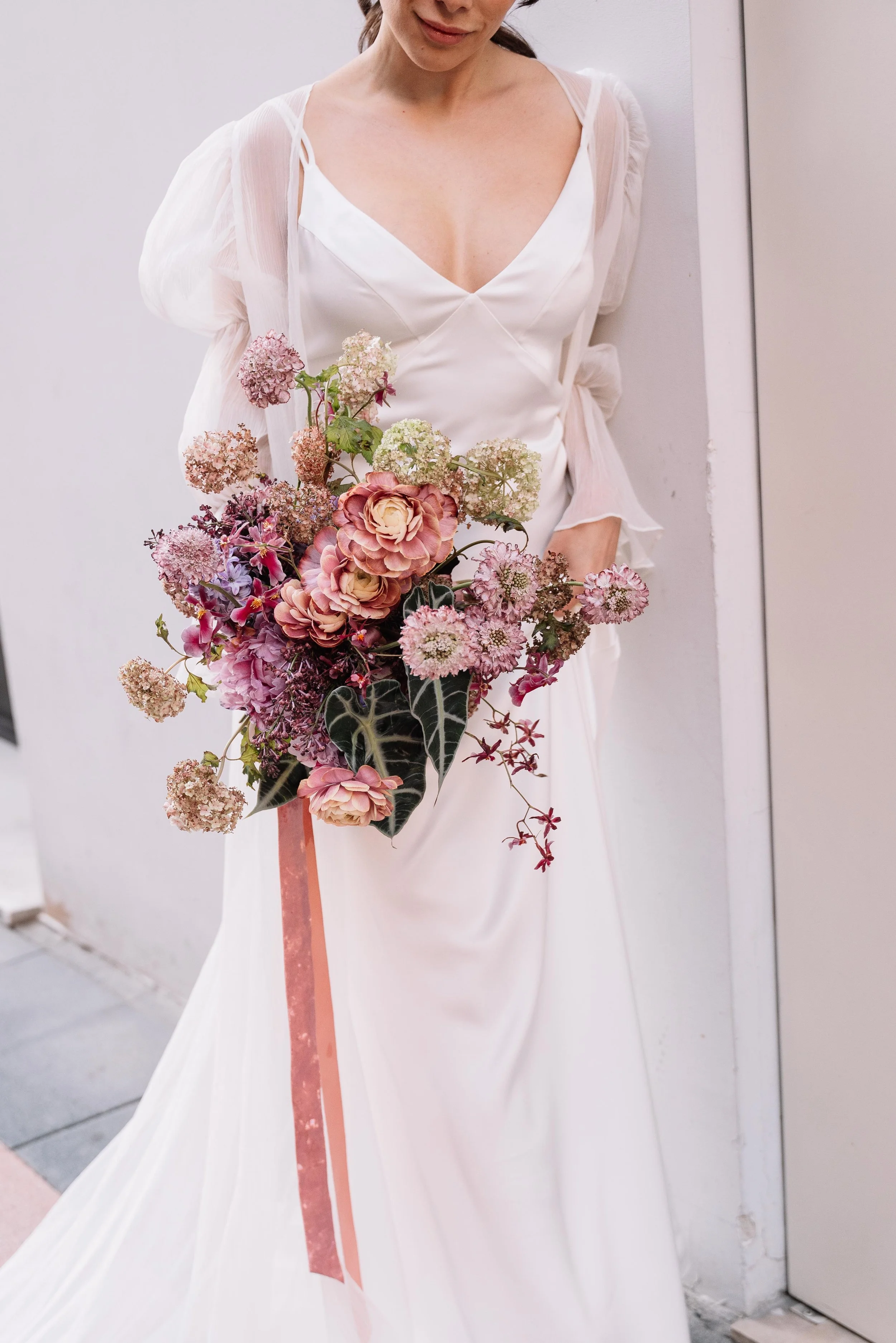 Mujer vestida con vestido blanco sujetando un ramo de flores en tonos rosas y verdes.