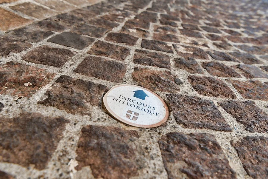 Photographie d'un signe Parcours Historique au sol, sur les pavets d'une  ancienne ruelle, à Mauguio.
