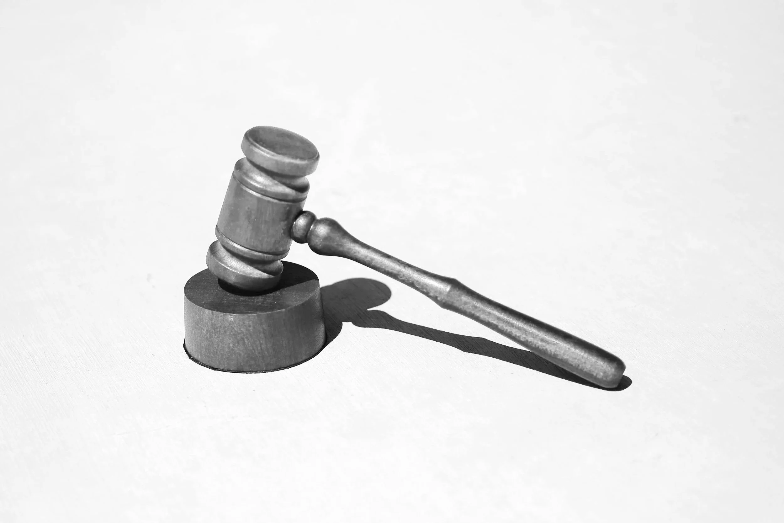 Black and white photo of a wooden gavel resting on a sound block with its shadow cast on a white surface.
