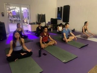 Members seated on yoga mats in a cross-legged position, practicing meditation, breathing exercises with Grace