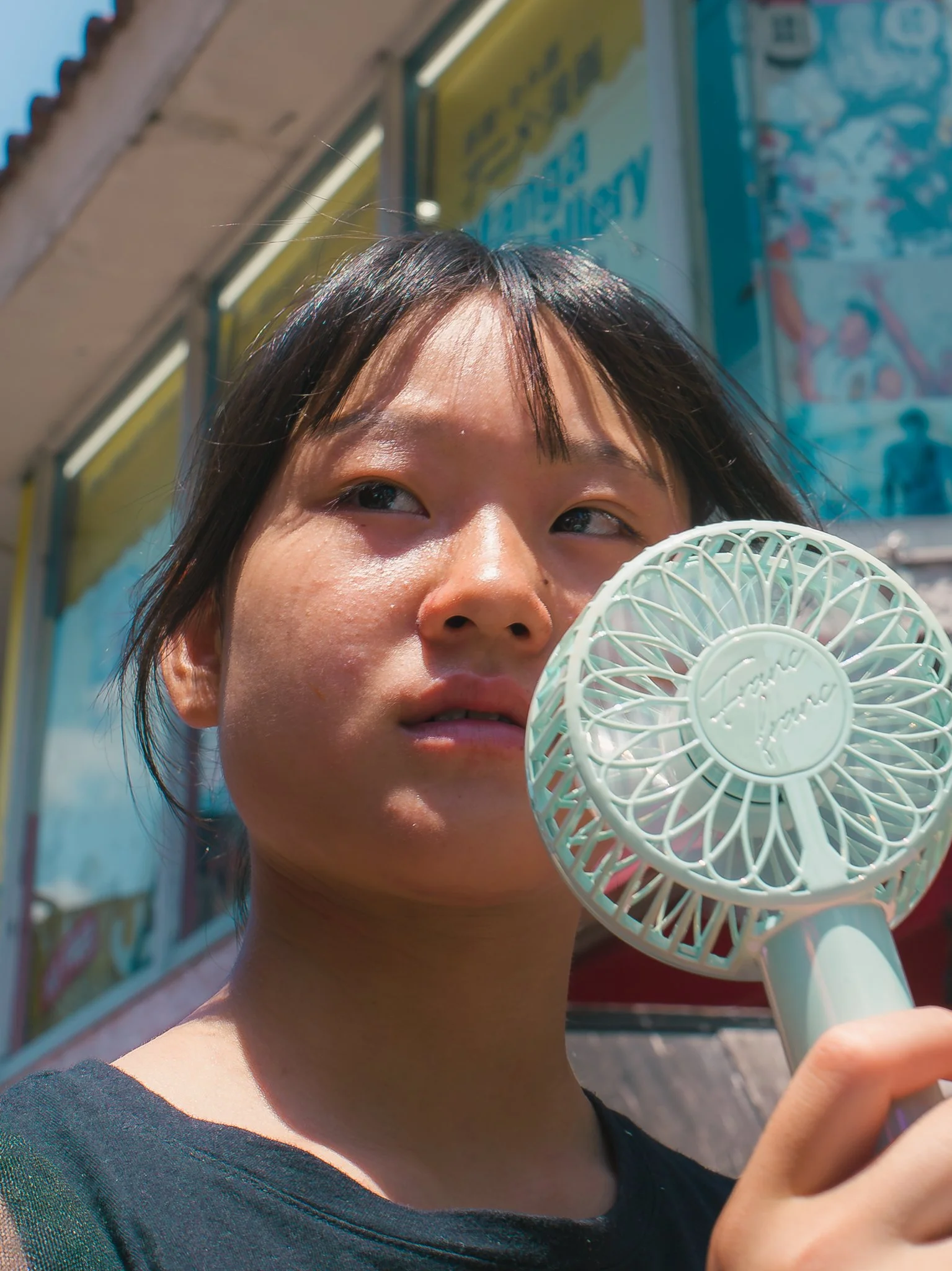 Close-up of a person with wet hair holding a small white portable fan near their face outdoors.