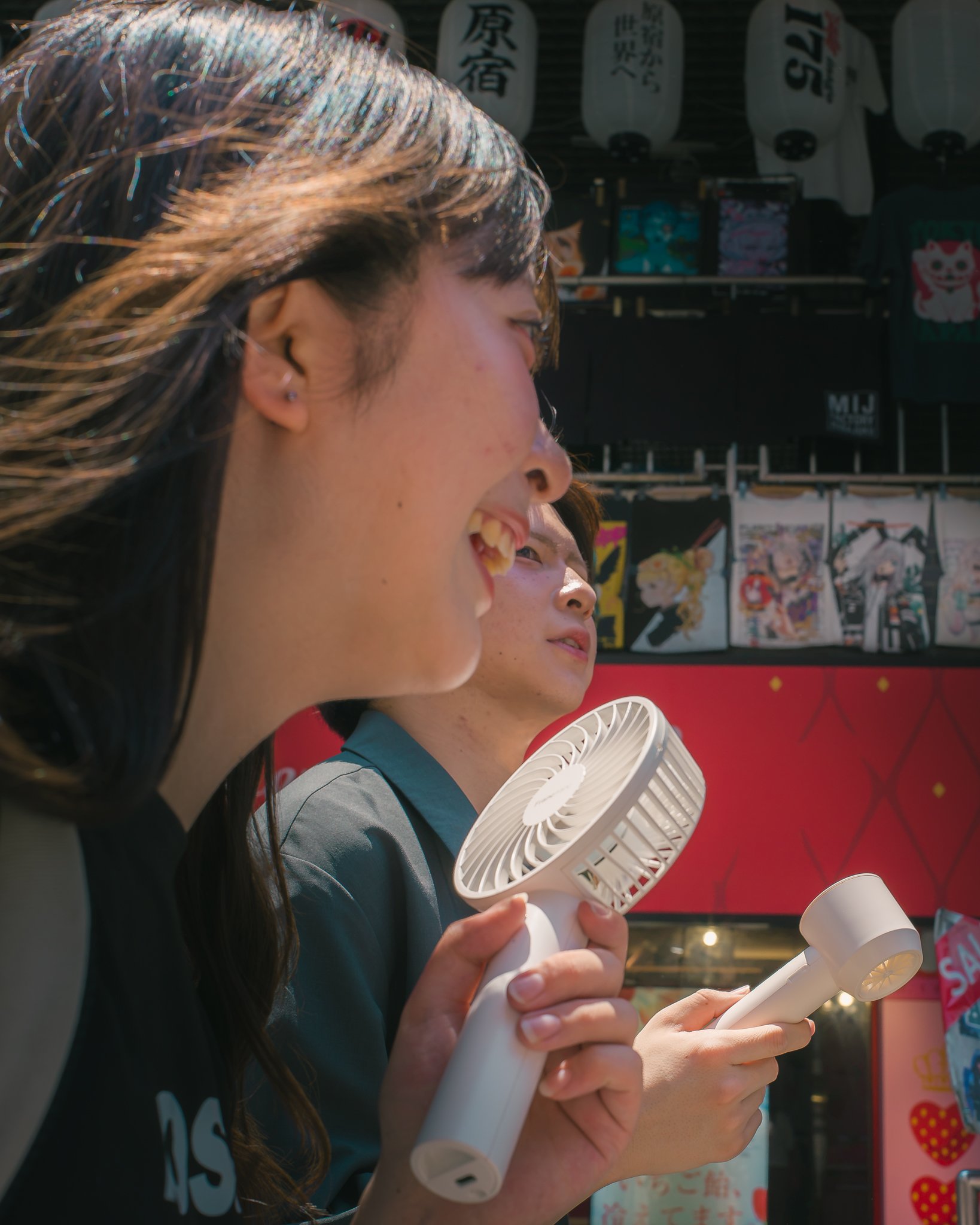 People holding portable handheld fans outdoors with Japanese lanterns in the background.