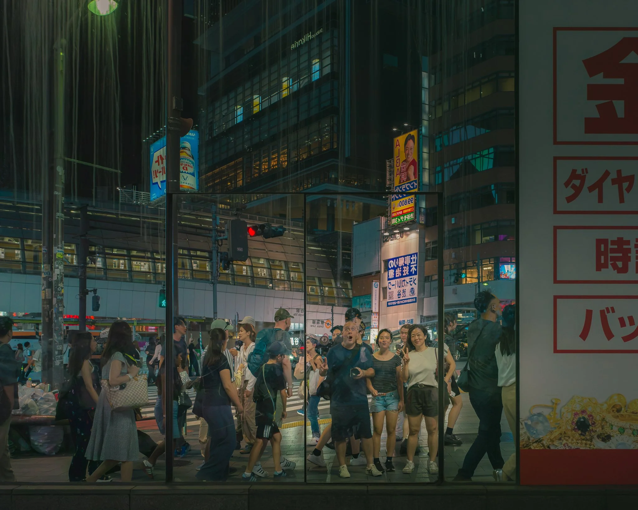 Pedestrians waiting at crosswalk in a busy city street at night, with illuminated billboards and neon signs in the background.