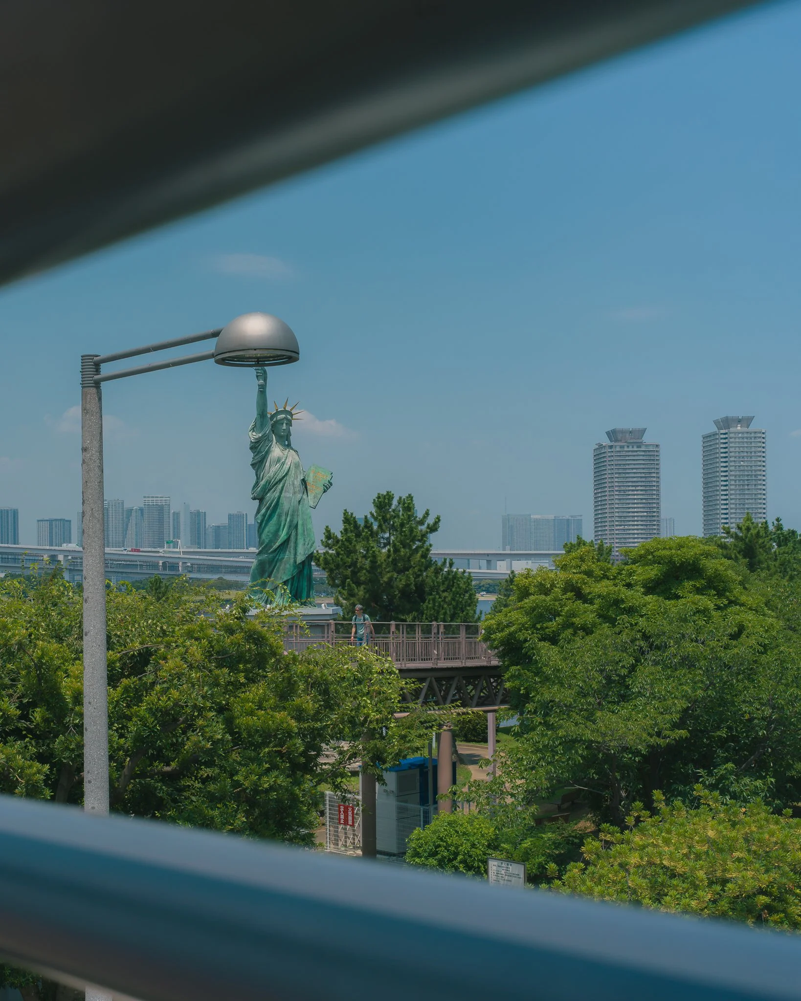 A view of the Statue of Liberty in New York City with modern buildings in the background, captured through an opening partially obstructing the bottom part of the image.