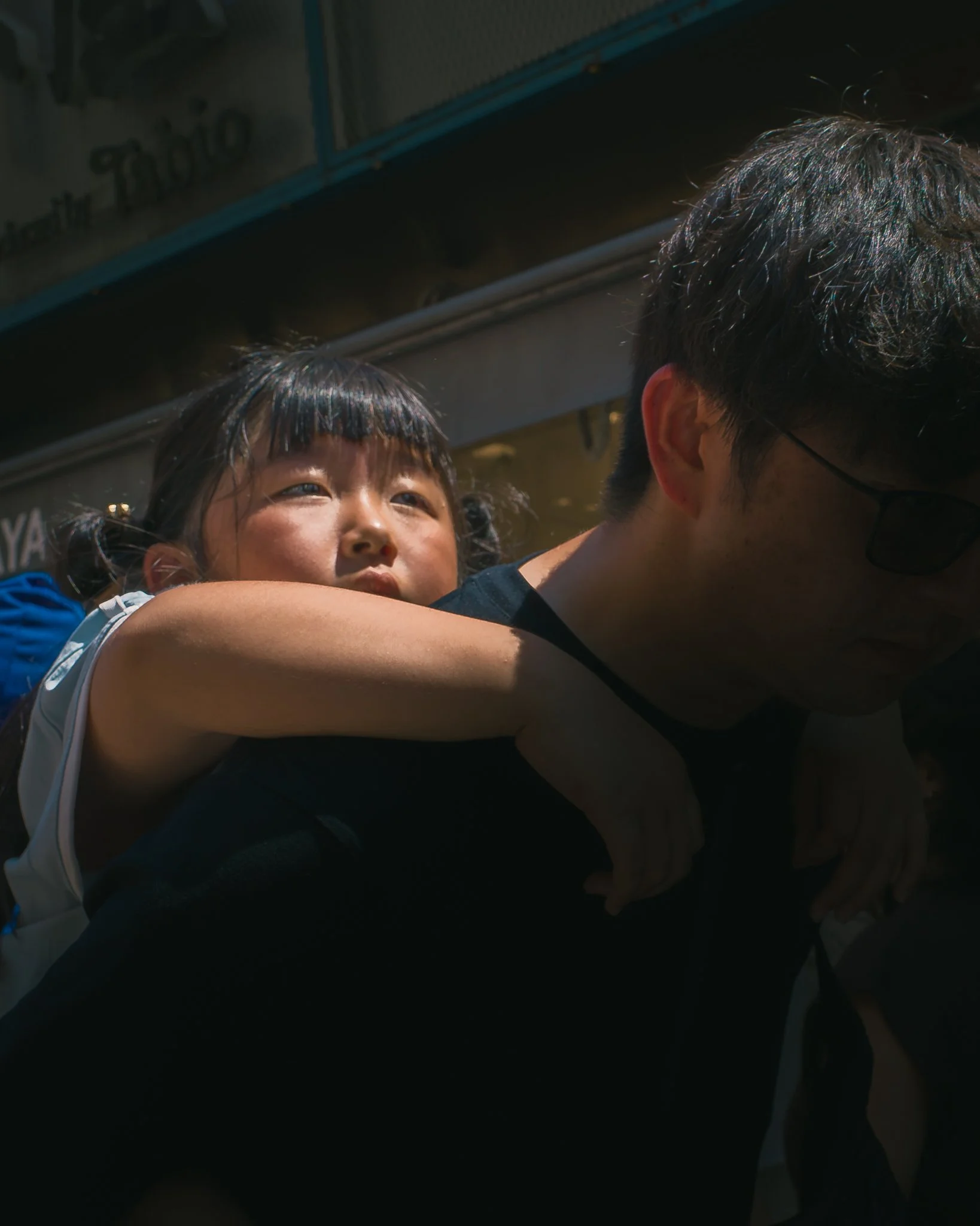 A young girl-looking up with a happy expression, being held or supported by a man with glasses, close to a body of water.